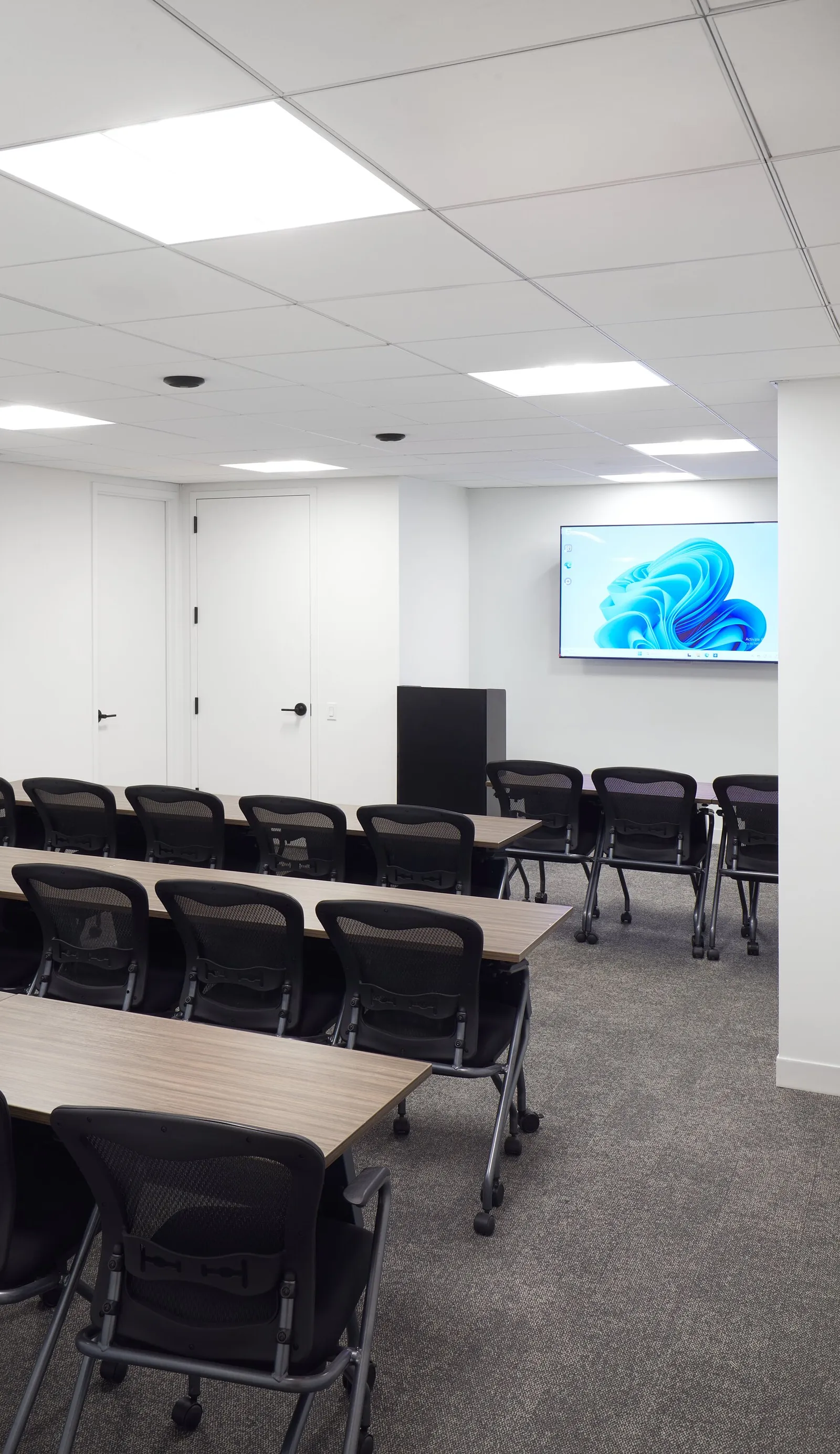 training room with long tables, black mesh chairs and a wall-mounted screen showing a blue design