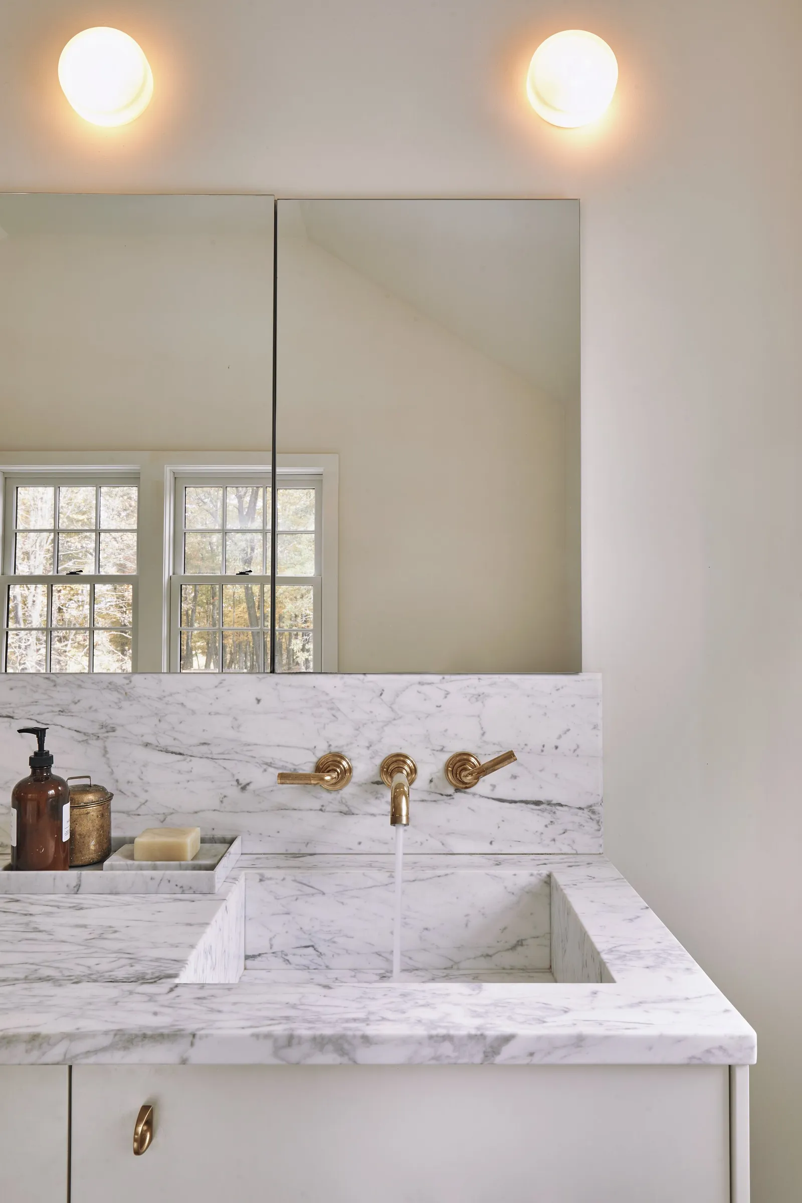 marble sink with wall-mounted brass faucet, mirror and two globe lights above