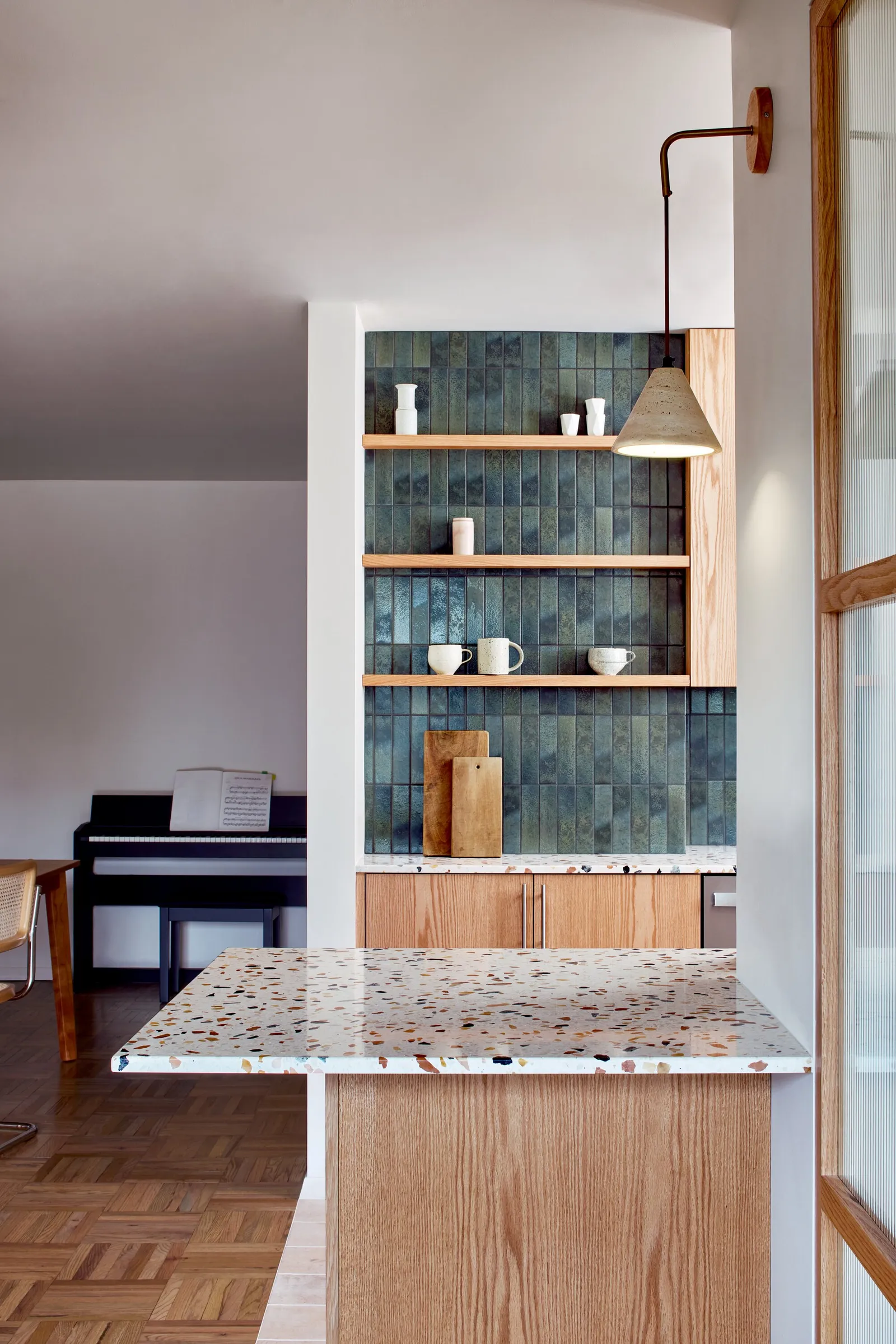 blue-green tiled shelves and a terrazzo counter, with an upright piano in the room beyond