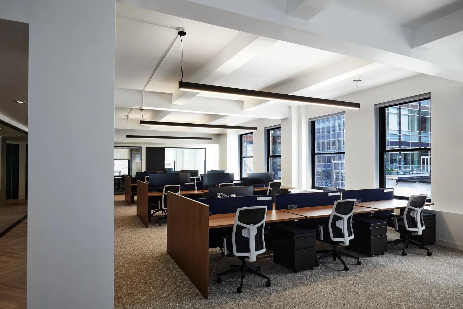 open office with walnut desks, navy dividers, white mesh chairs and tall windows under pendant lights