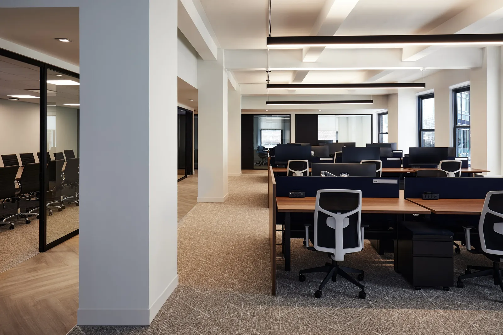 open office from behind a white column, rows of desks and a glass meeting room at left