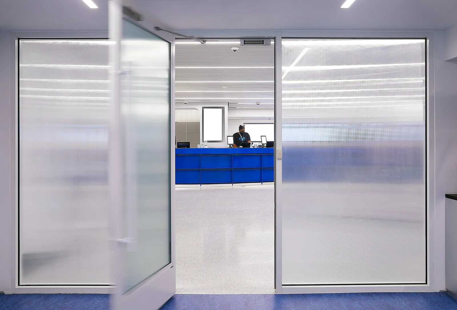 frosted glass double doors, one swung open, with the blue counter visible beyond and a blue floor in front