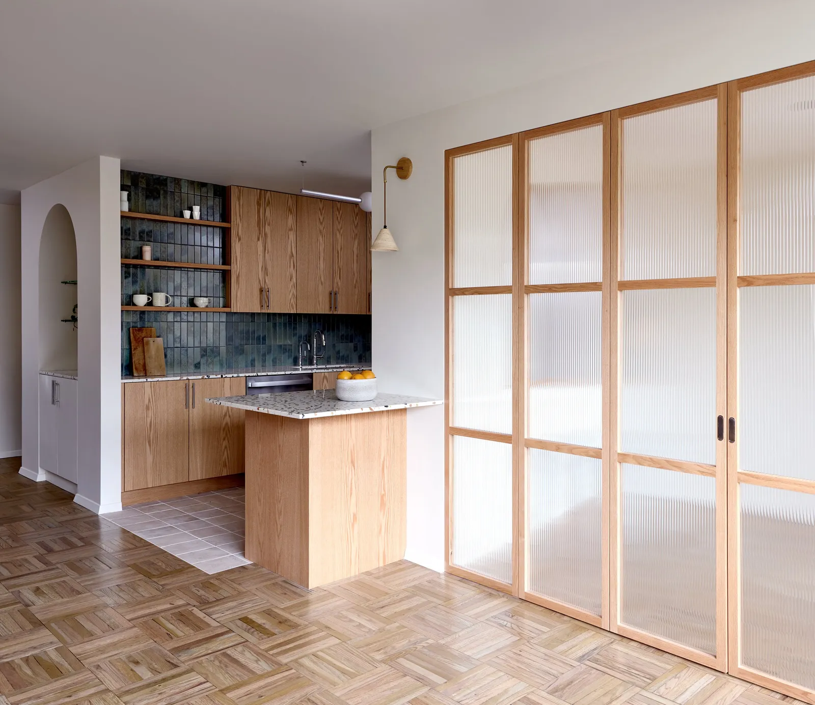 wall of fluted-glass and wood doors with the kitchen peninsula to the left and an arched niche