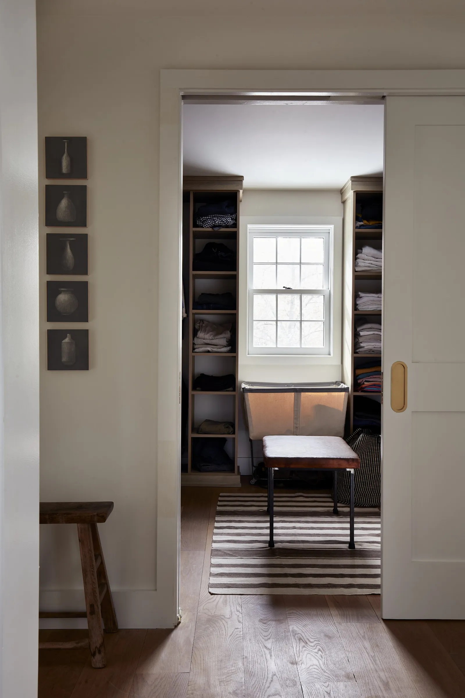 view through a sliding door to a walk-in closet with shelves and a striped rug, with a row of small vase prints beside it