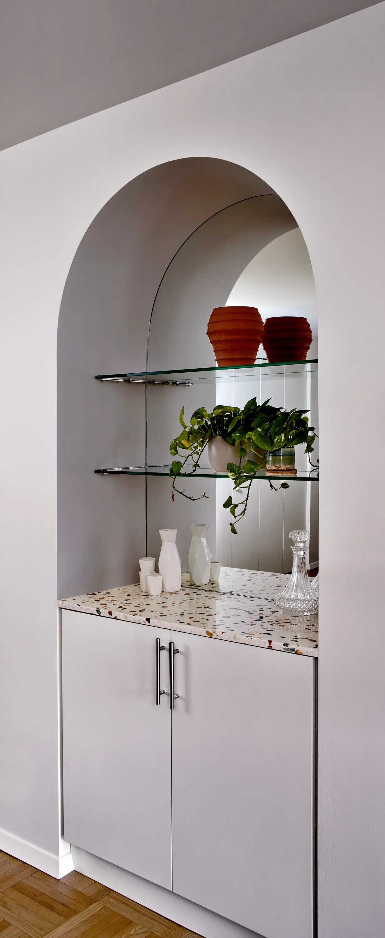 arched niche with glass shelves, a plant and terracotta vases above a white cabinet