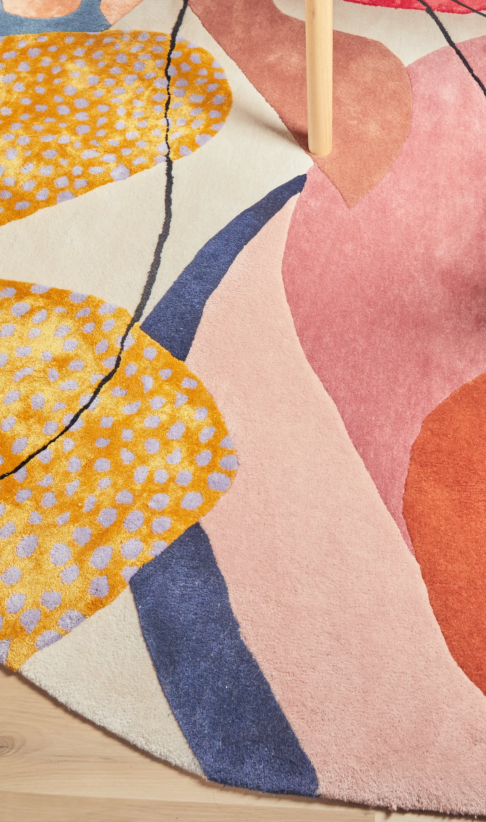 rug detail with yellow dotted shapes, navy and pink forms on cream, wood floor at bottom edge