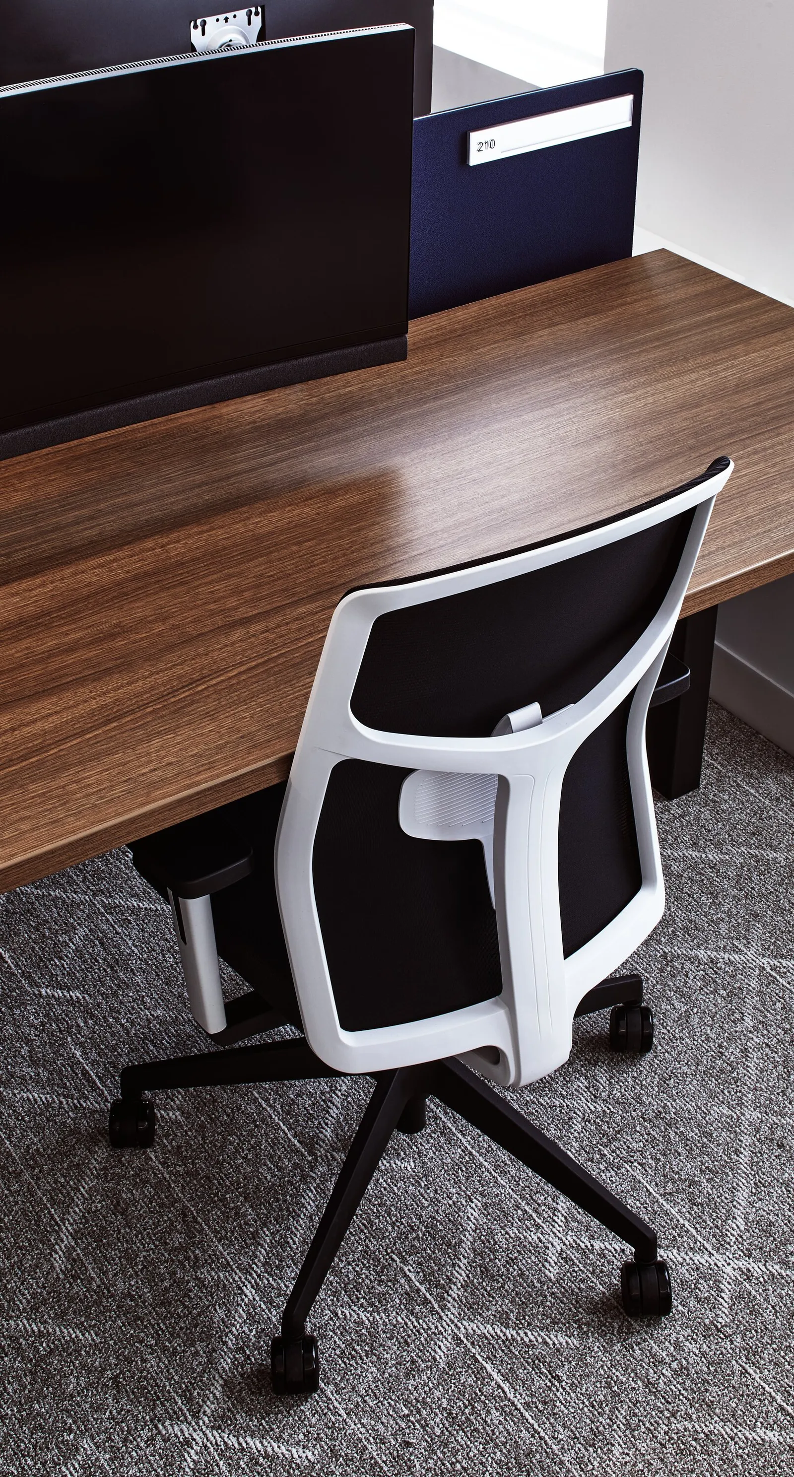 white mesh task chair pulled up to a walnut desk, dark monitor and blue divider above