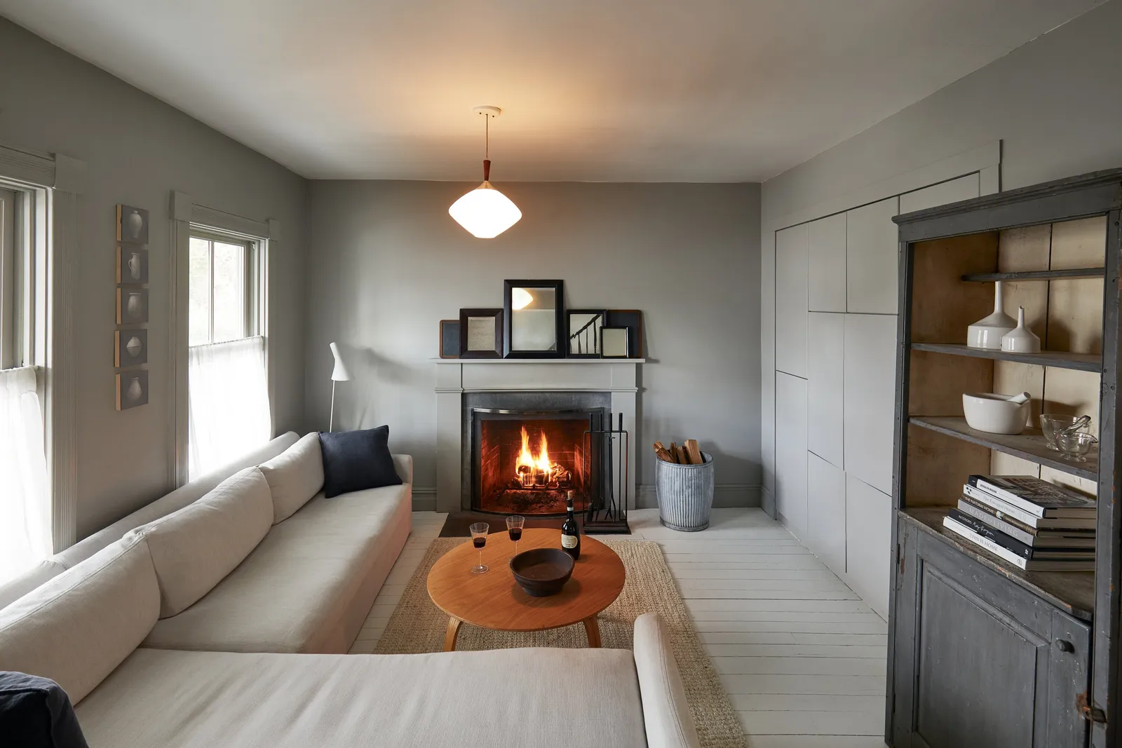 living room with a long cream sofa, a round wooden coffee table and a lit fireplace on gray walls