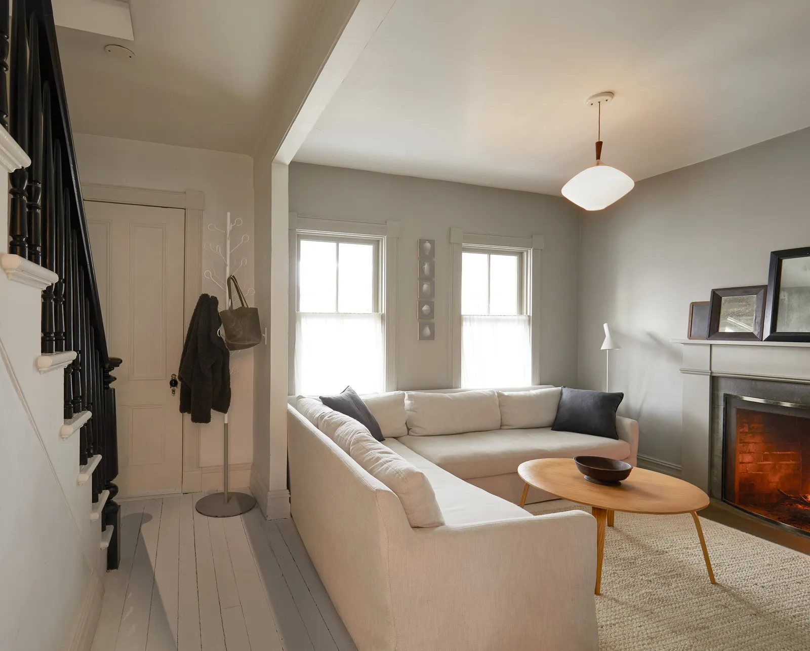 entry and living room with black stair railing, a cream sectional, an oval wooden table and a lit fireplace