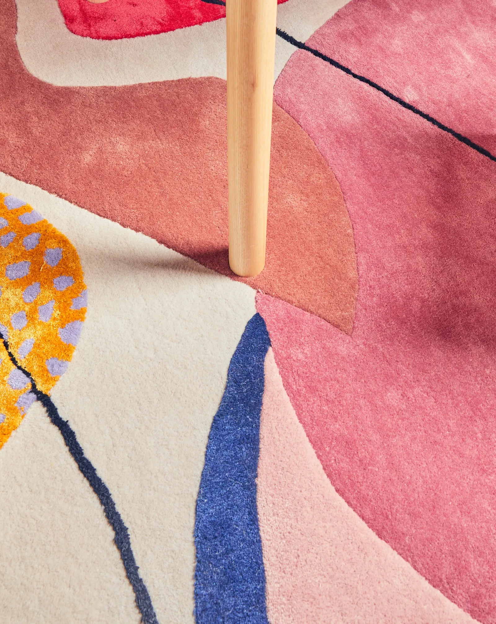 close crop of a wooden table leg standing on a pink, cream and blue patterned rug