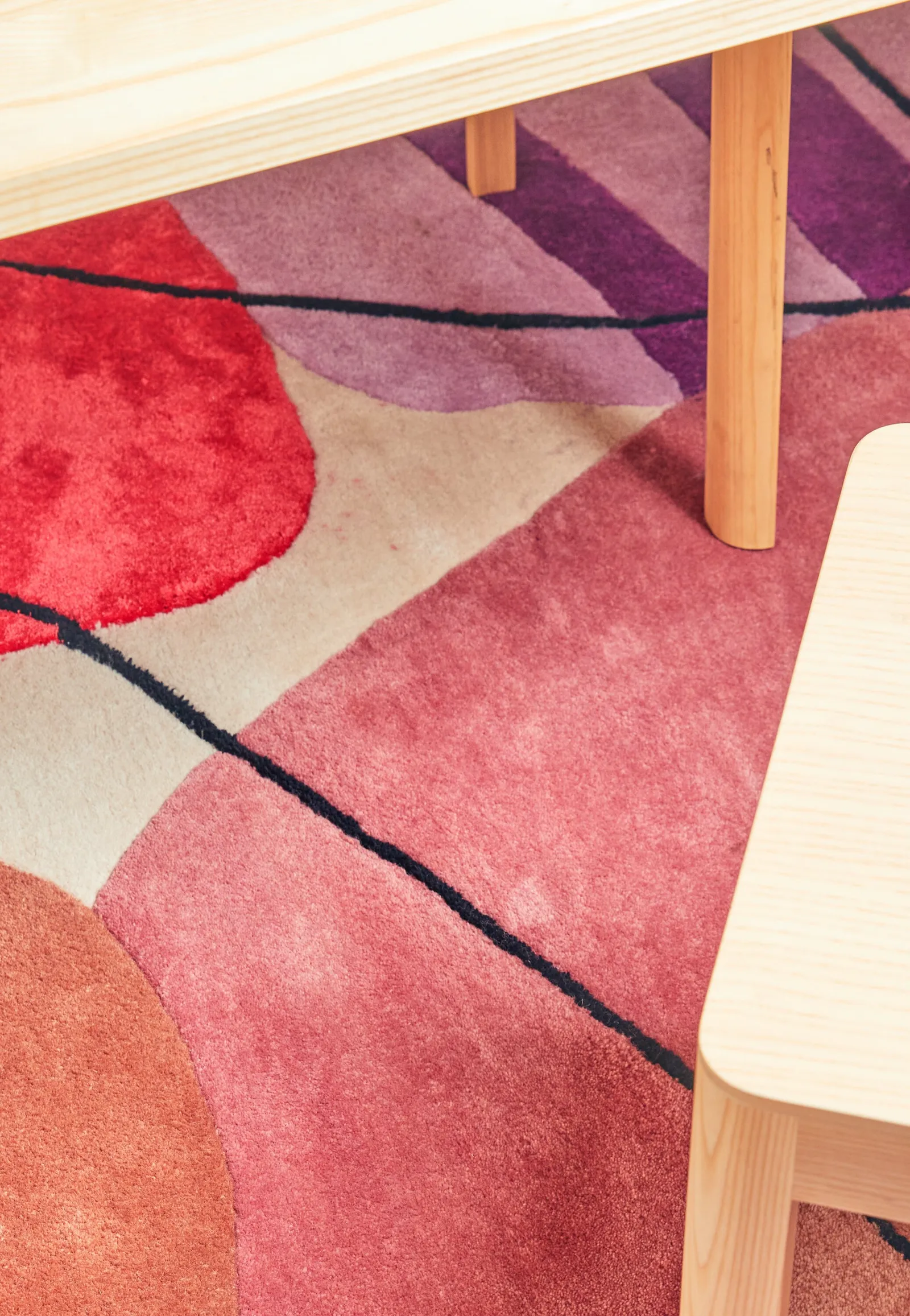 wood table legs over a rug of red, pink, purple and cream shapes with dark line
