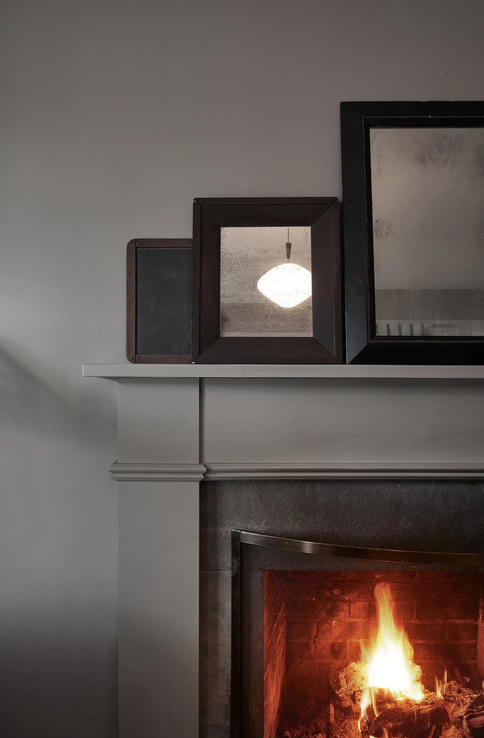 detail of a gray mantel holding dark framed mirrors above a glowing fire