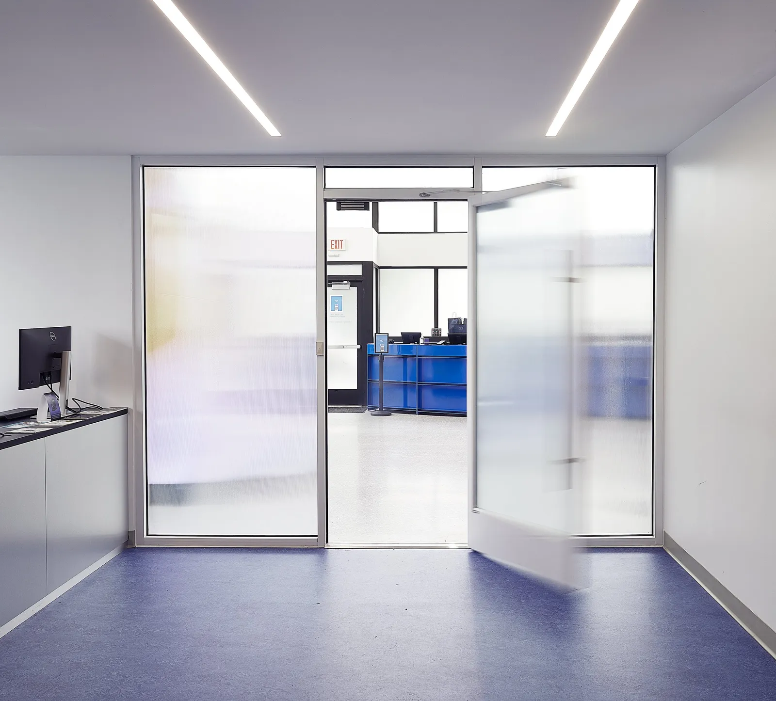 entry vestibule with frosted glass doors, a desk at left, a blue floor, and the shop visible through the doorway