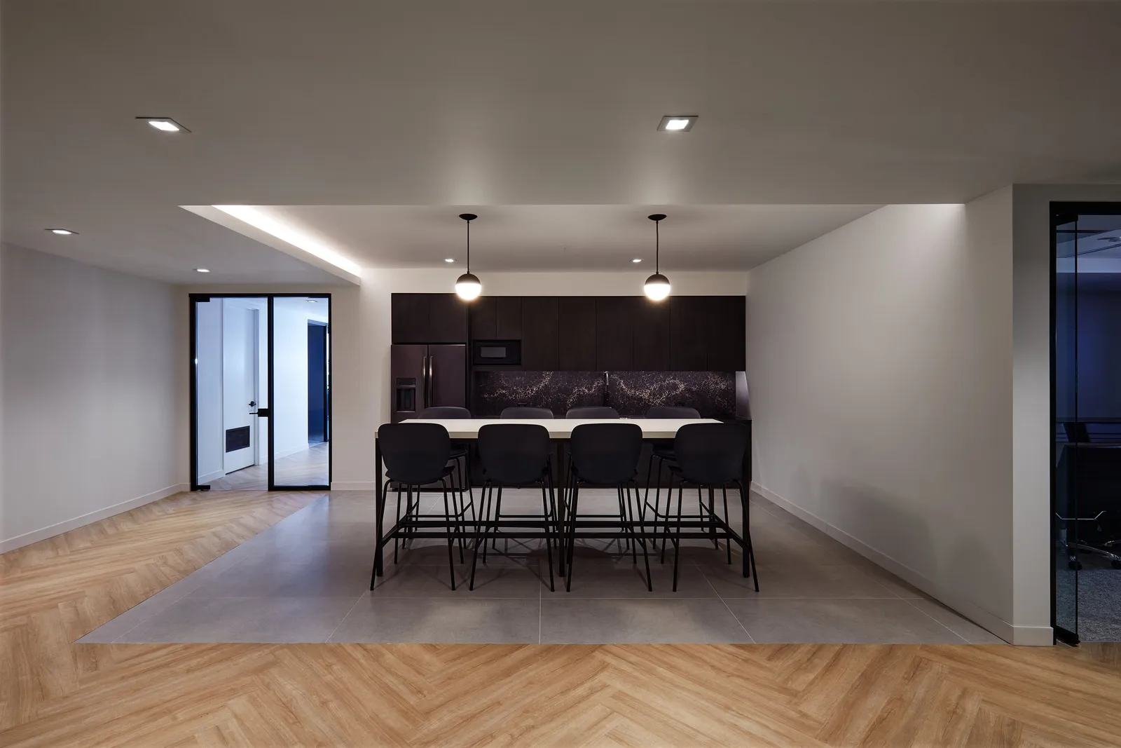kitchen area with high table and black stools, dark cabinets, two globe pendants on a stone-gray floor panel
