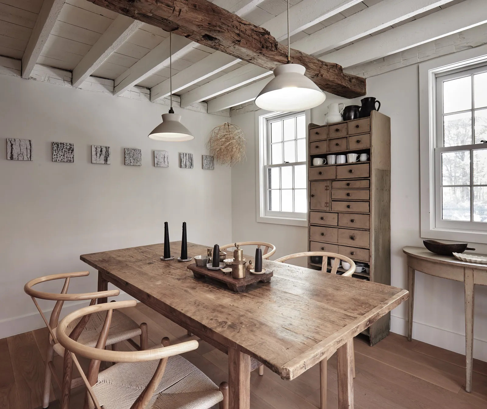 rustic wooden dining table with wishbone chairs, a wooden cabinet of small drawers and two pendant lamps