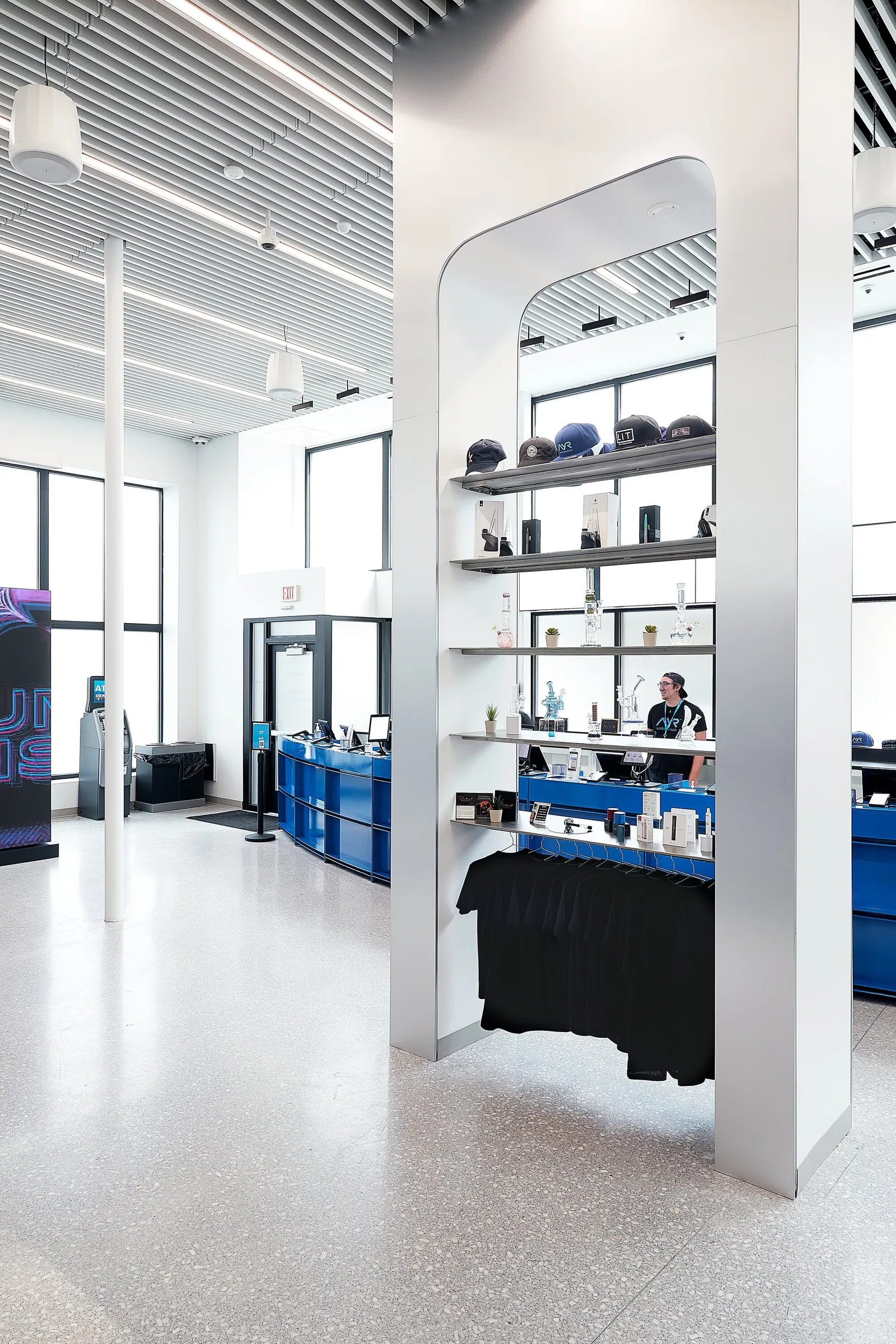 tall view of a white arched display column with caps on shelves and clothes, the curved blue counter behind
