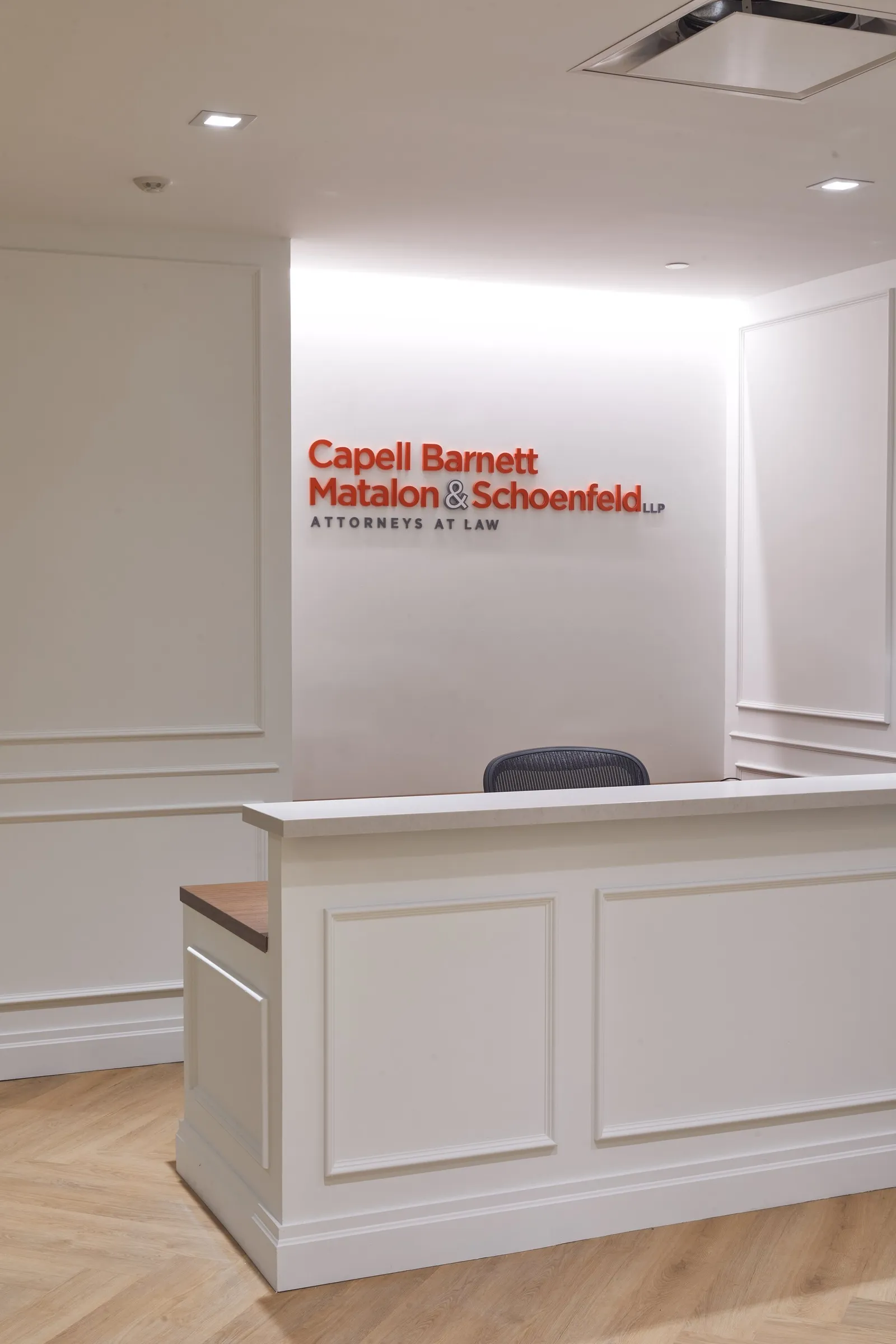 reception desk with white paneling, dark chair behind it and red firm name on the wall behind