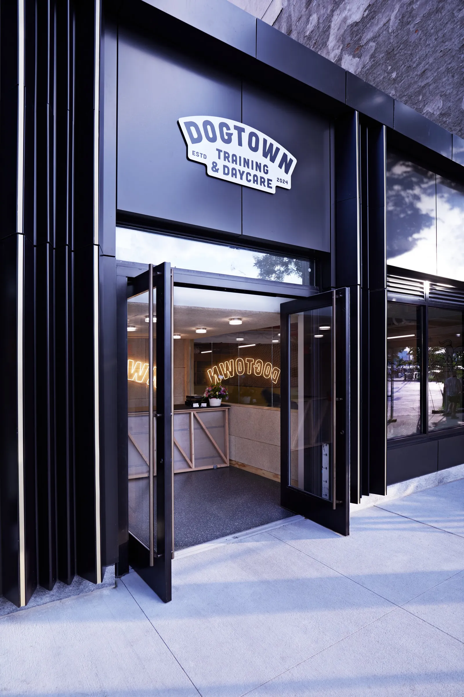 vertical view into the black storefront through open glass doors, the neon sign glowing inside