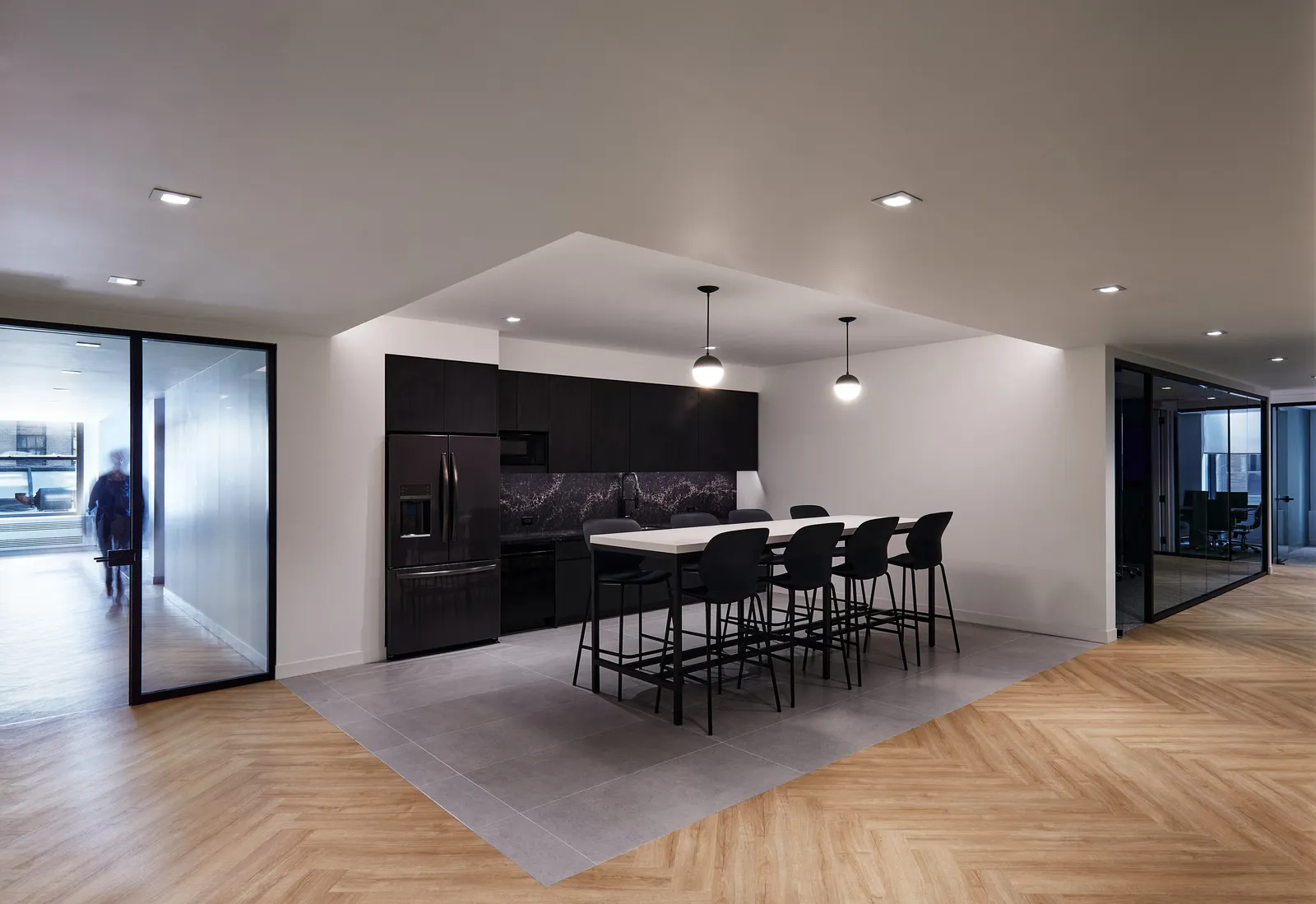 same kitchen from the side, a distant figure beyond glass at left and glass walls at right