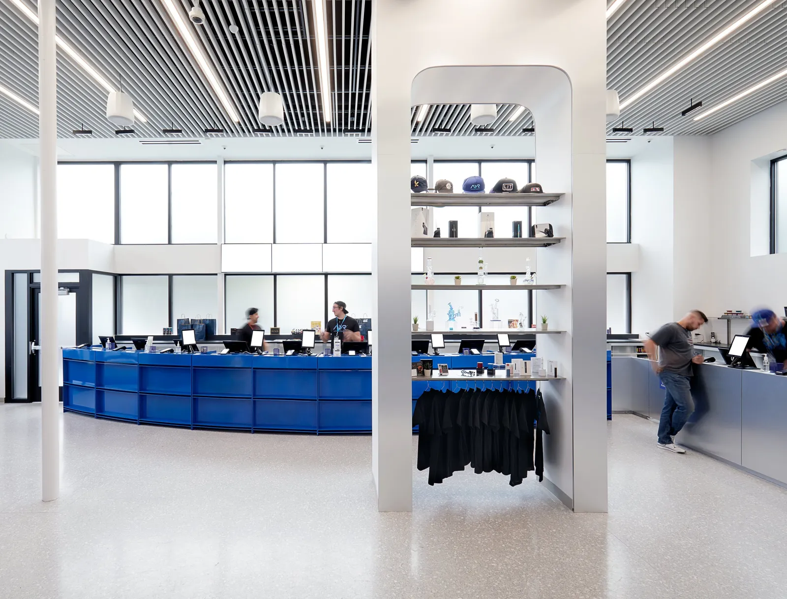 high-ceilinged shop with a display column in front of the curved blue counter, a customer leaning at right