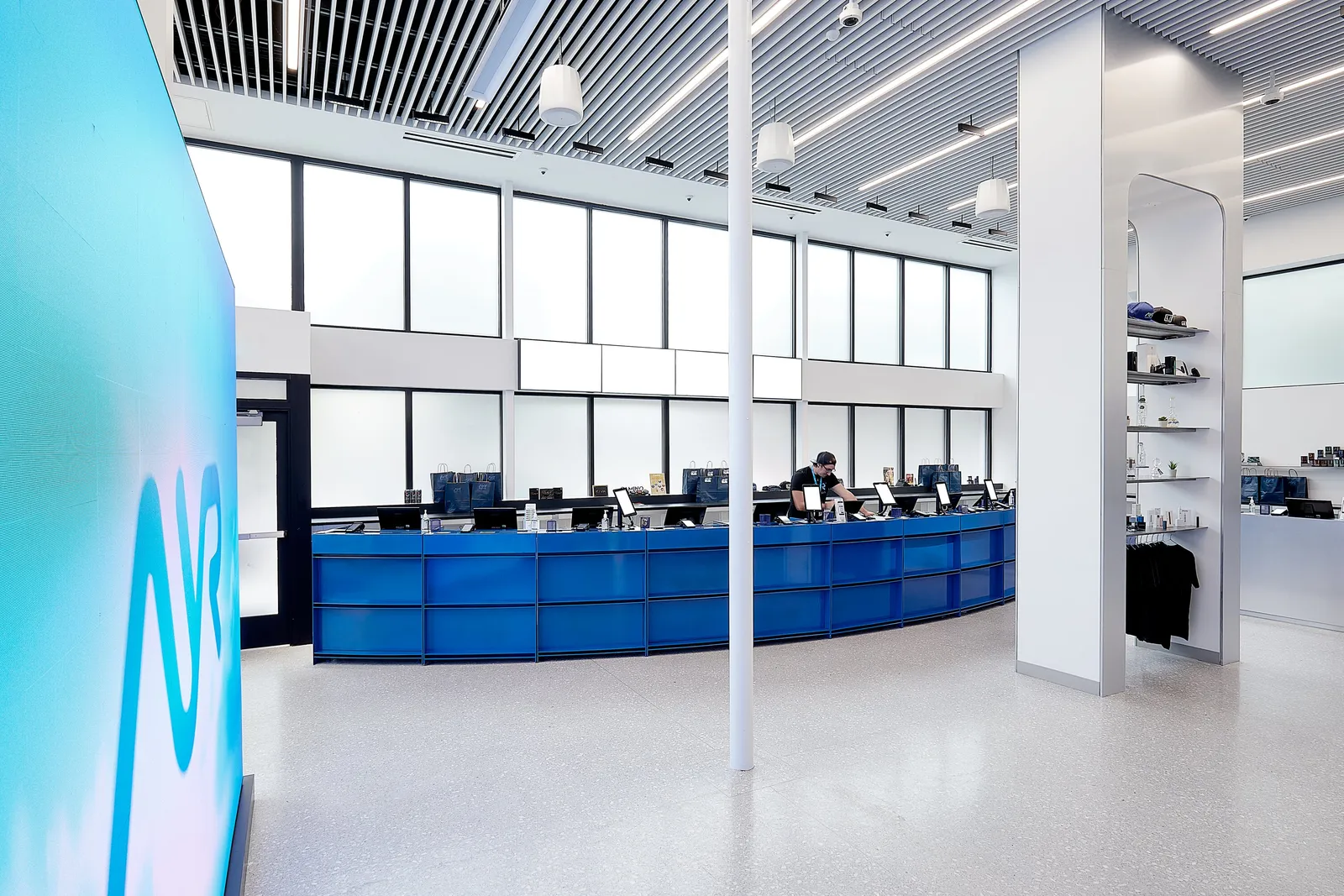 glowing turquoise AYR sign wall at left, a white column and the curved blue counter across a pale floor