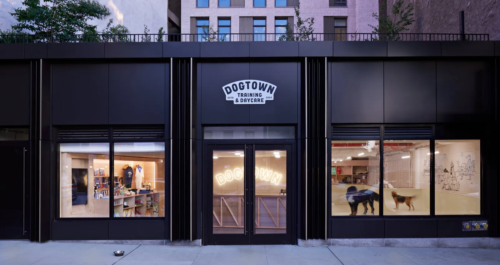 wide view of the black storefront at dusk, with the sign over the door and two windows showing the shop and dogs