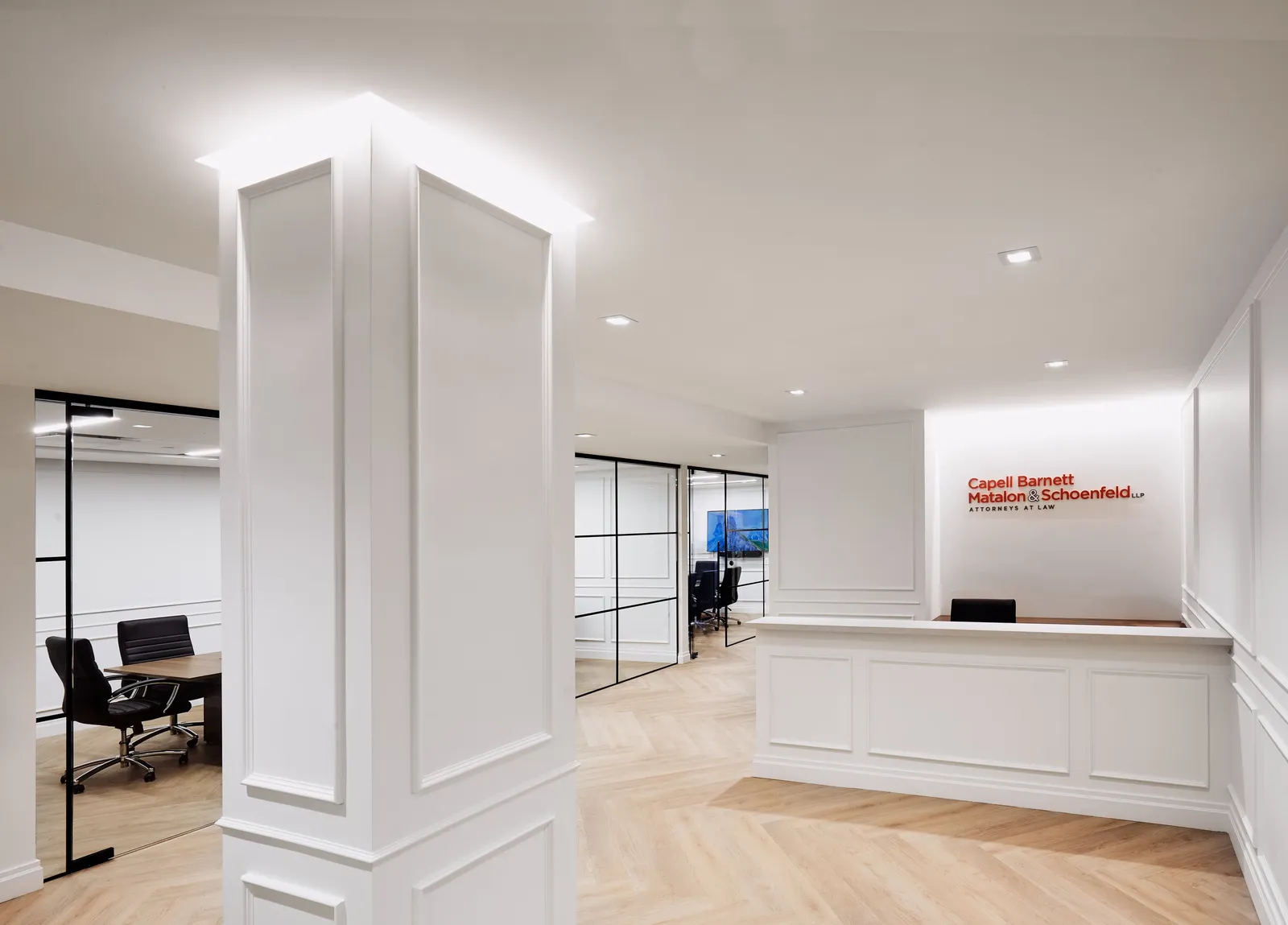 reception with a white paneled column, front desk and red firm name on the wall, glass offices at left