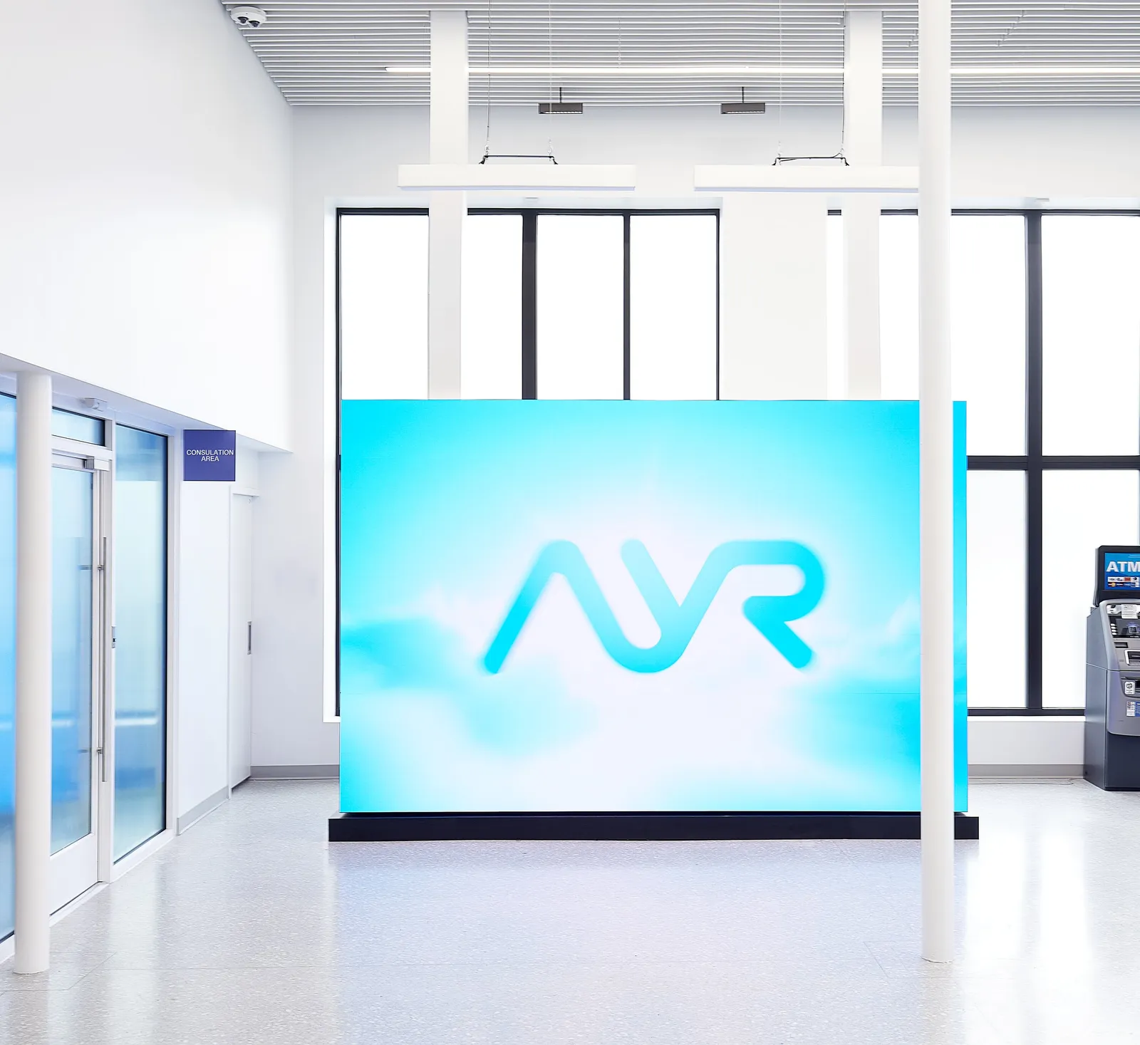 turquoise AYR sign standing in front of tall black-framed windows, with an ATM and glass doors at the side