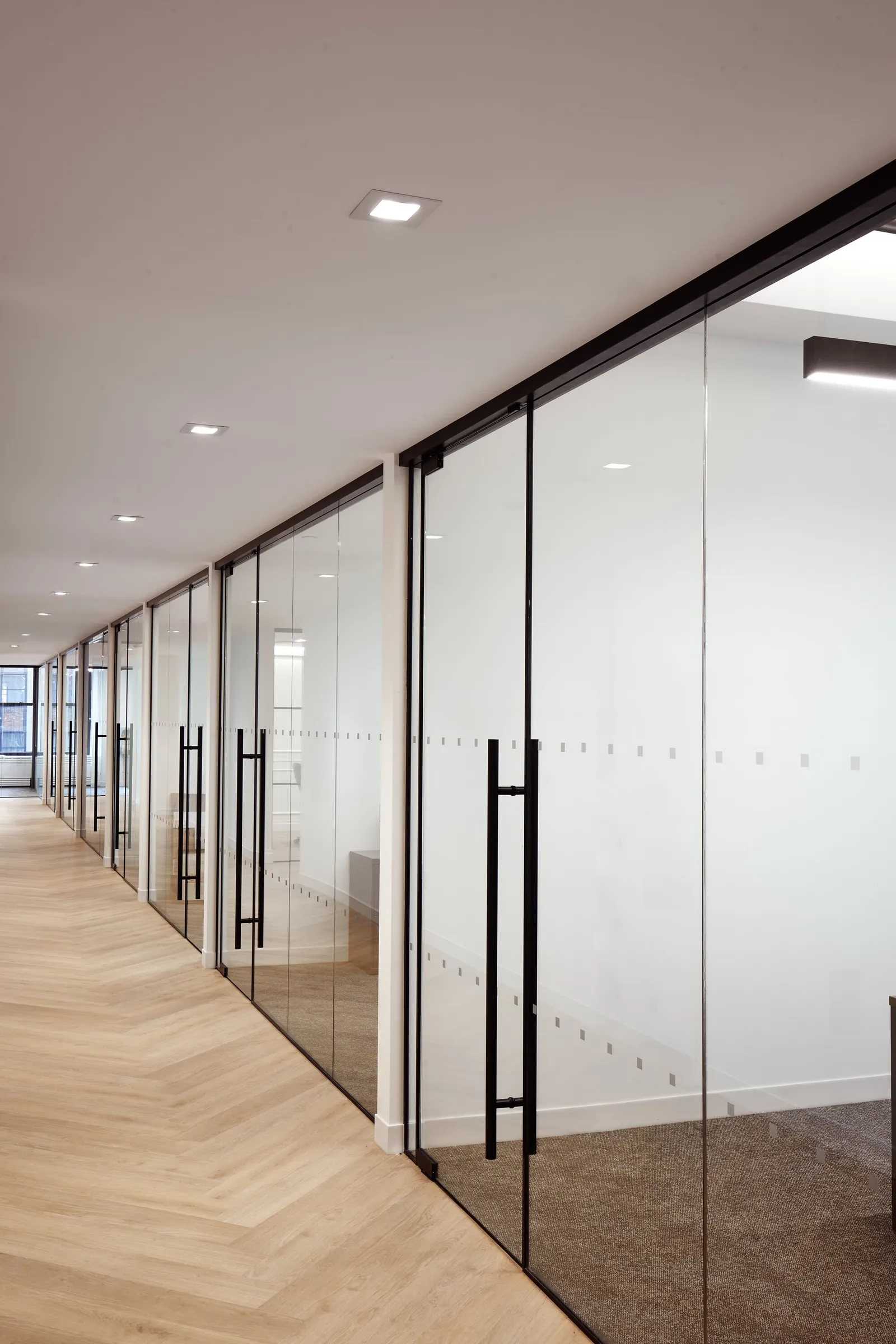 corridor of frameless glass office doors with black pull handles and dotted privacy film