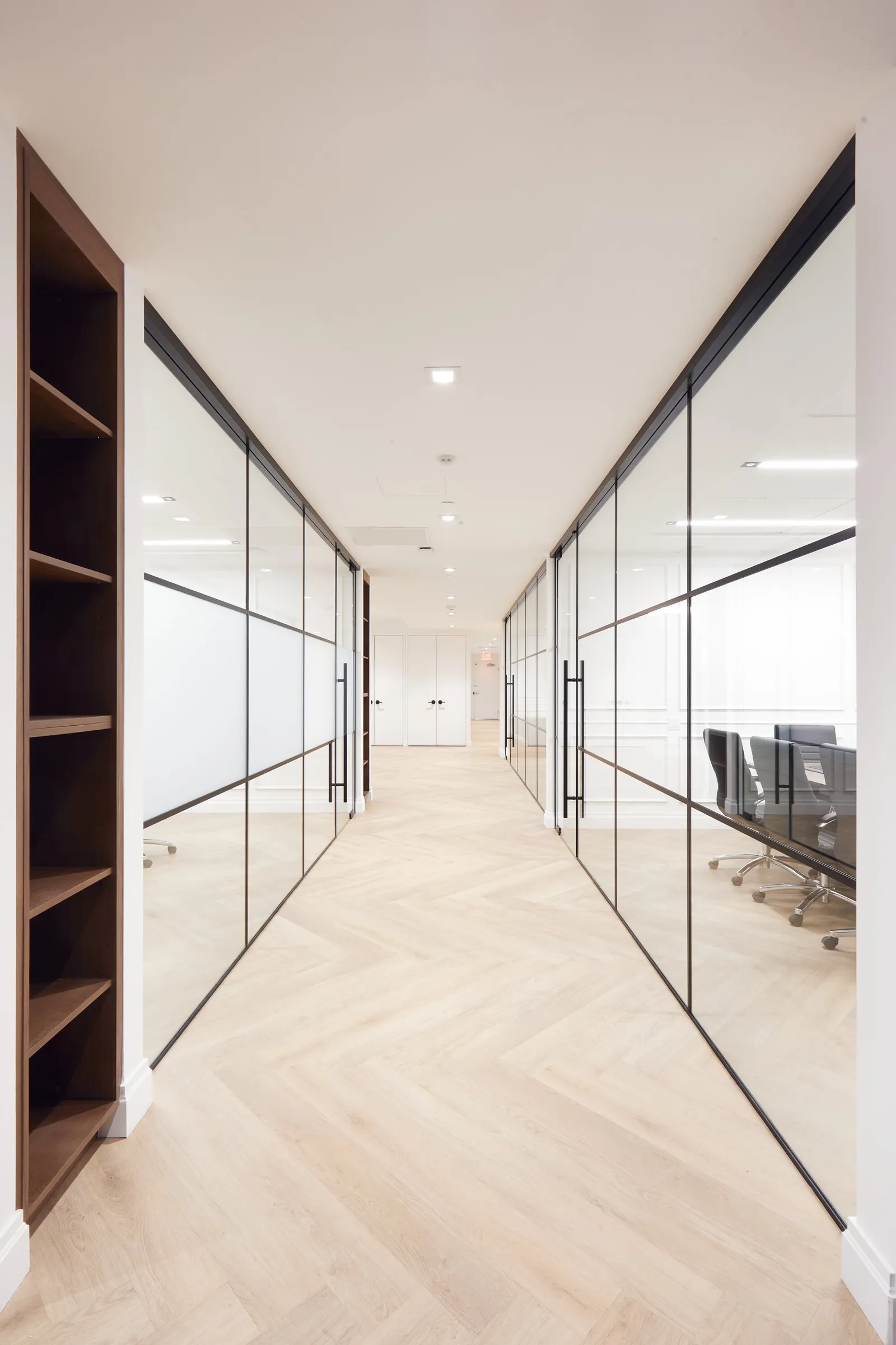 corridor between glass walls and a walnut bookshelf, white double doors at the far end