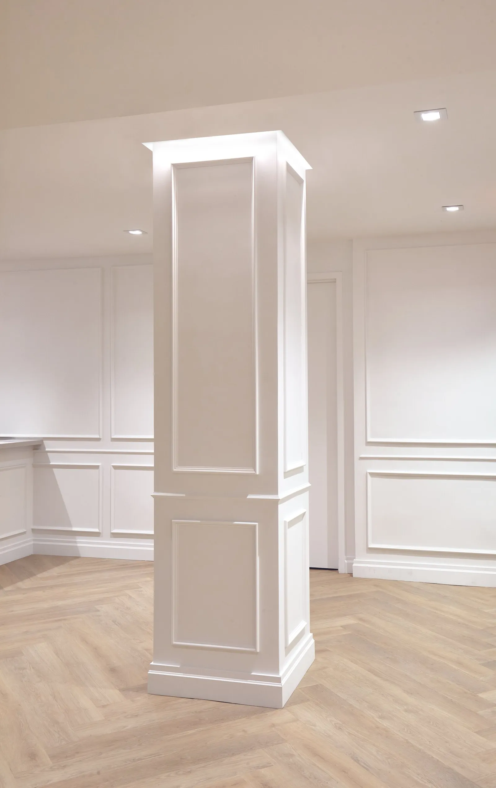 white paneled square column with recessed lights standing in an open room with herringbone floor
