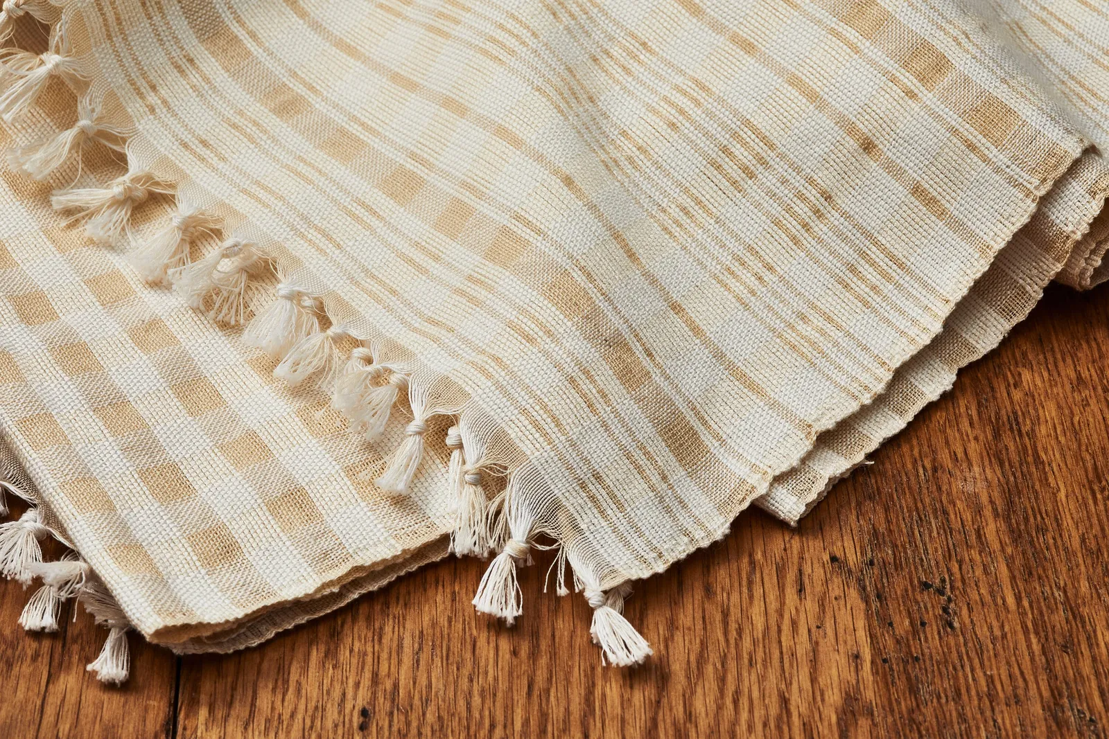 cream woven cloth with pale gold checks and stripes and knotted tassels, laid on a dark wood surface