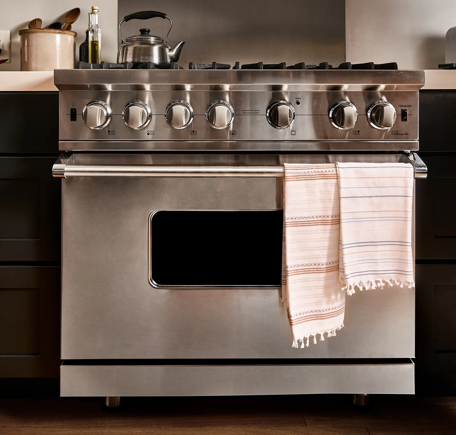 stainless steel range with a striped pink and cream tea towel draped over the oven handle, a kettle on top, in a dark kitchen
