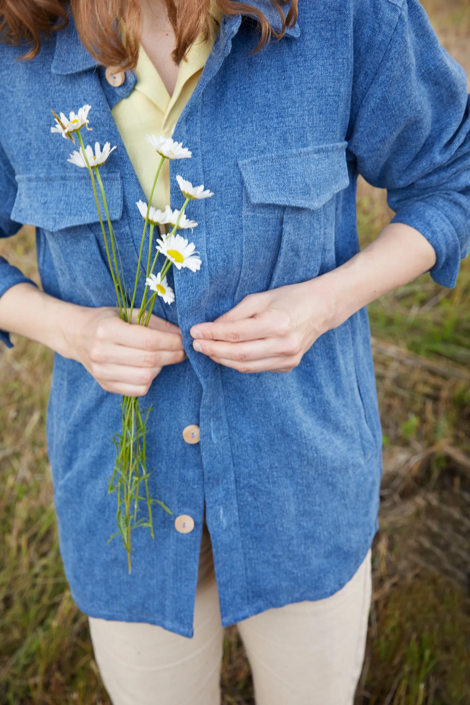 close crop of a person in a blue shirt jacket holding a small bunch of white daisies at the chest