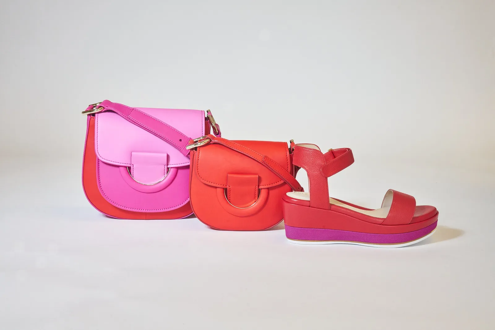 a pink-and-red saddle bag, a smaller red bag and a red platform sandal with a purple sole, lined up on gray