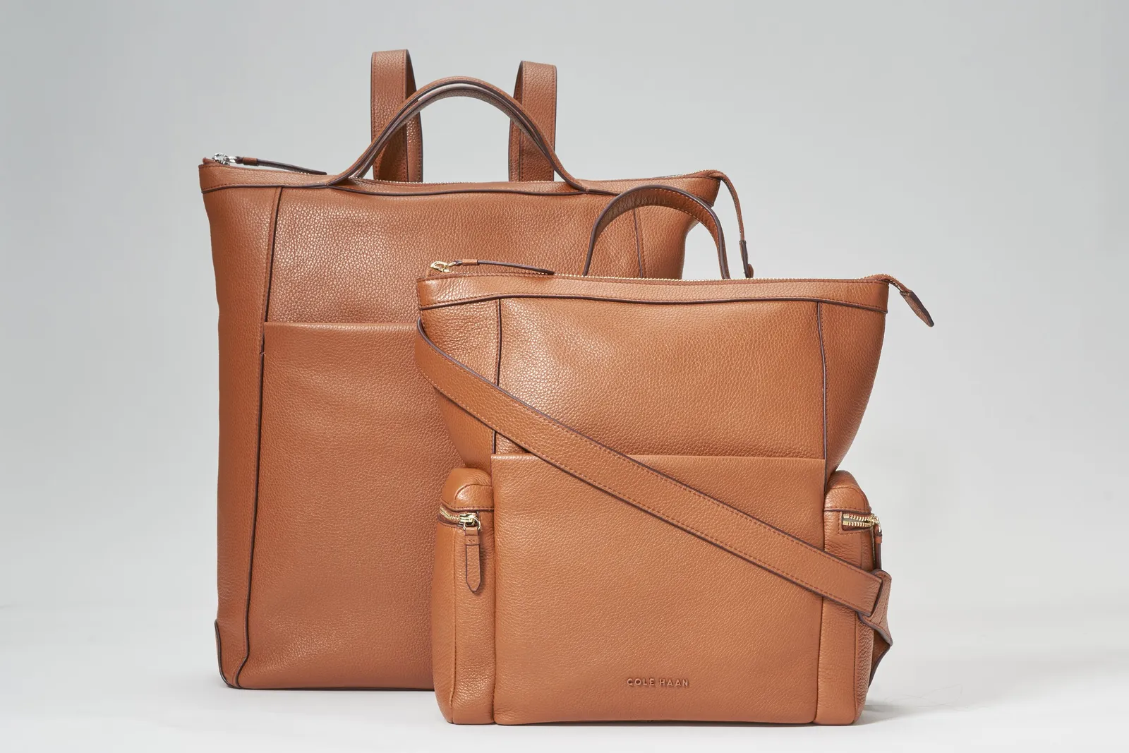 two tan pebbled-leather bags, a tall tote-style backpack behind a smaller crossbody bag with a long strap