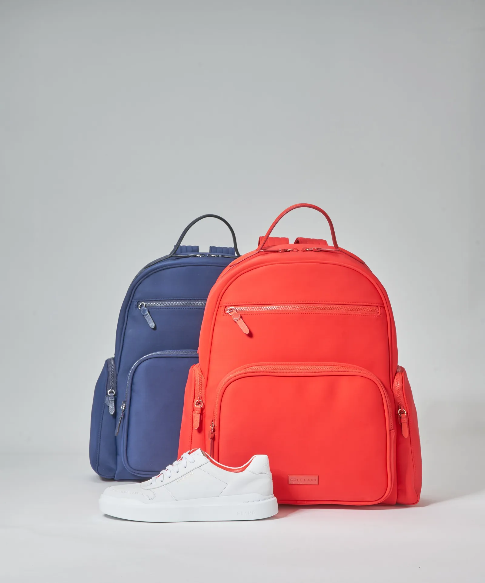 a navy nylon backpack beside a bright red backpack, with a white leather sneaker in front