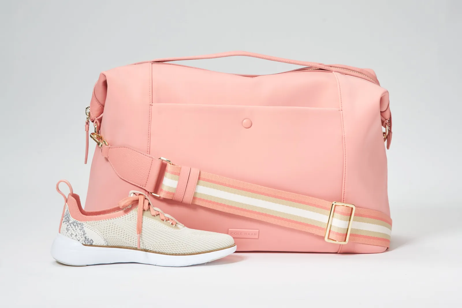 a soft pink duffel bag with a striped cream and pink strap, and a pink and cream knit sneaker beside it