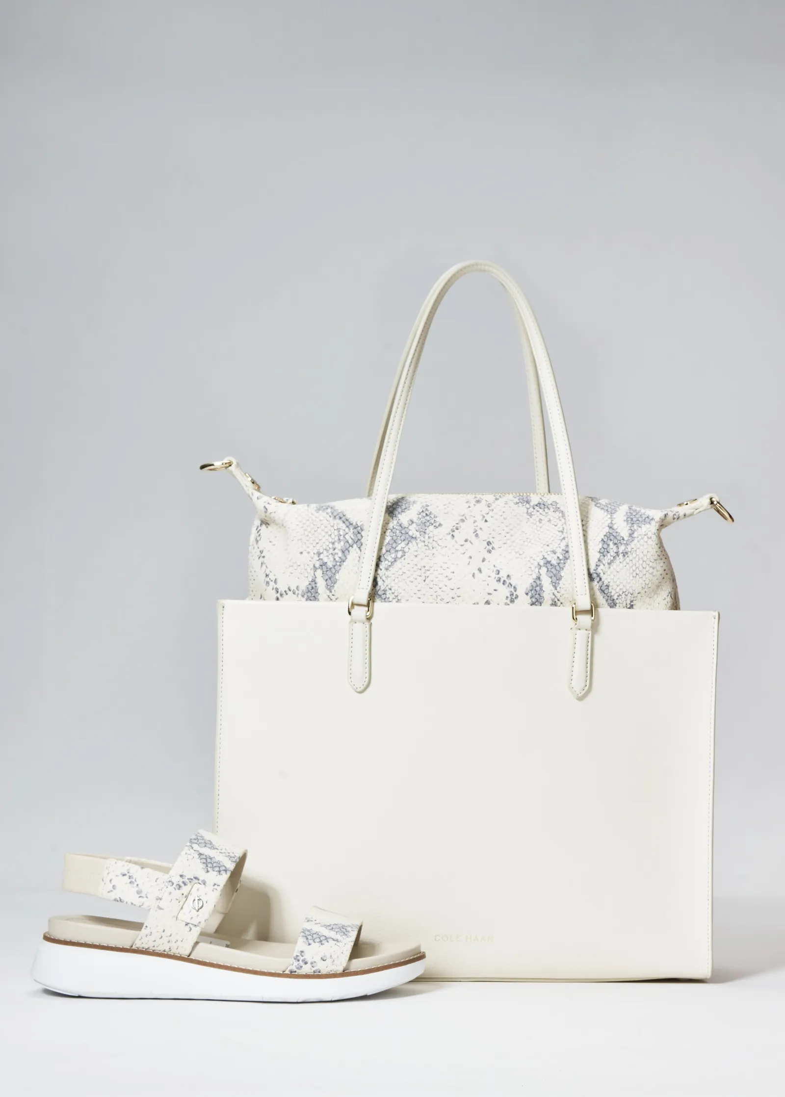 a tall cream tote with a snakeskin-print bag peeking out behind it and a white snakeskin-trim sandal at its base