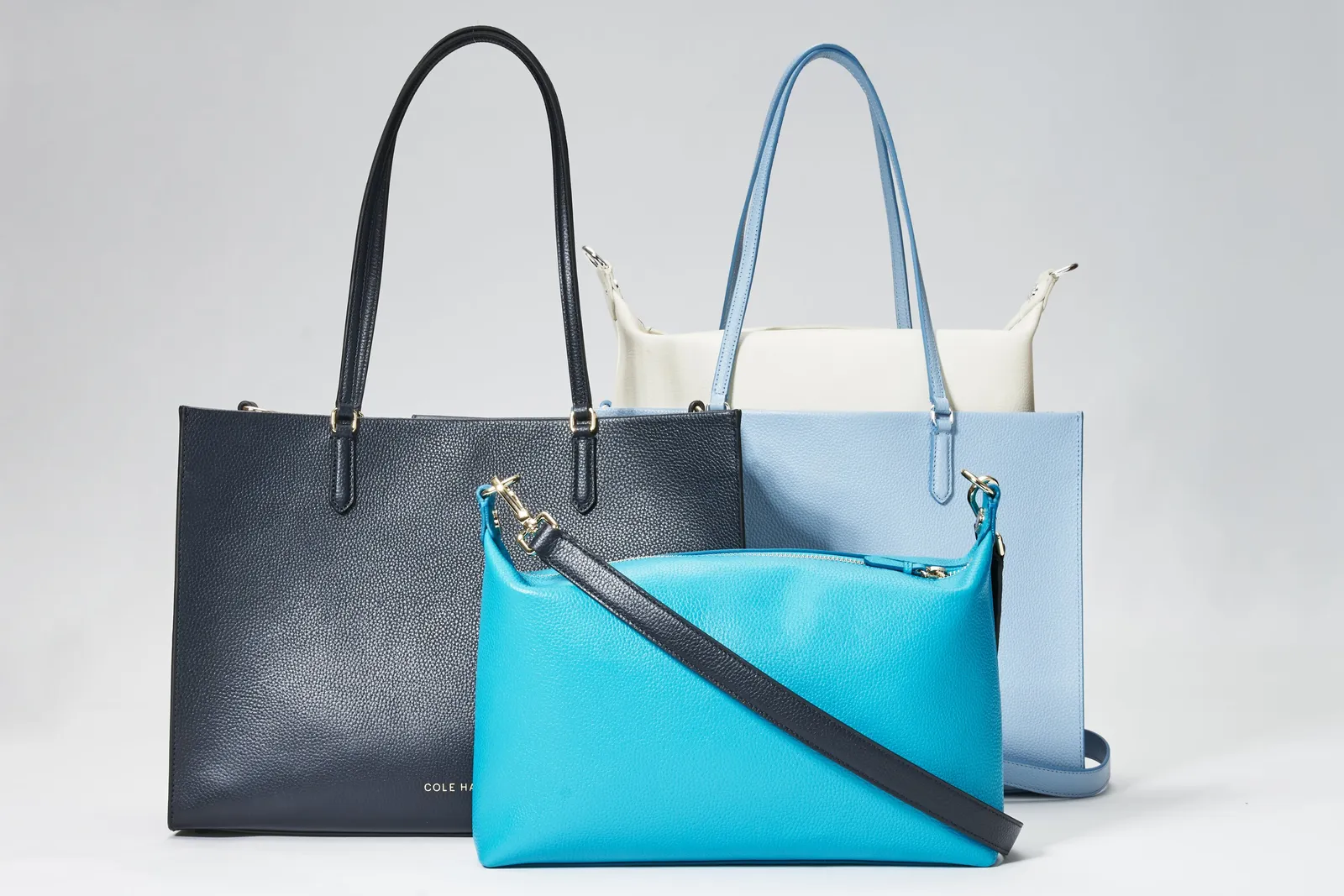 navy, light blue and cream totes grouped behind a bright turquoise crossbody bag with a dark strap