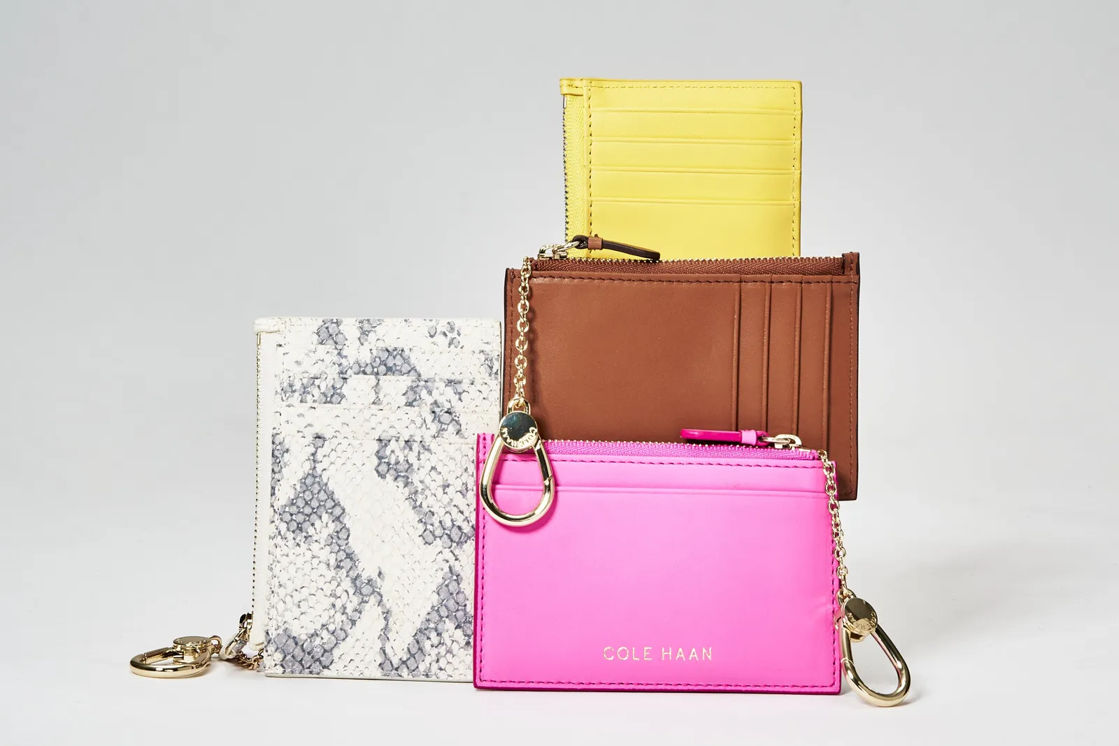 four card holders stacked in a cluster: yellow, tan leather, snakeskin print and hot pink with gold clips