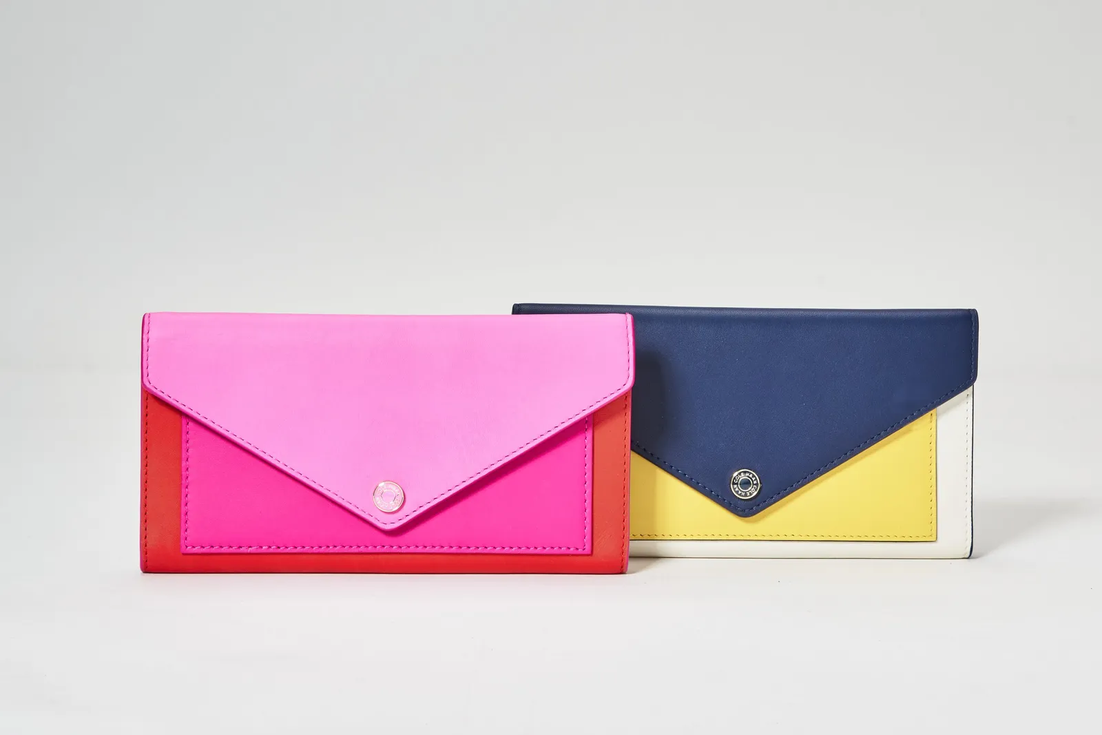 two envelope wallets side by side, one hot pink and red, the other navy, yellow and white
