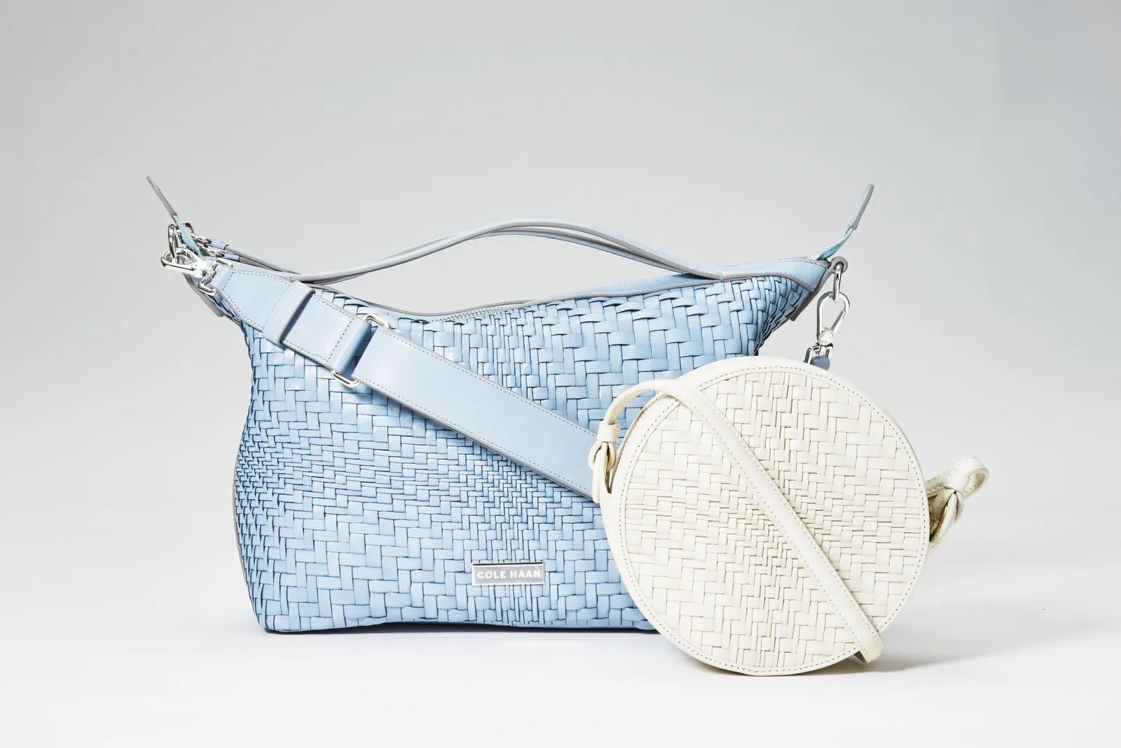 a pale blue woven shoulder bag with a wide strap, with a round white woven crossbody bag leaning against it