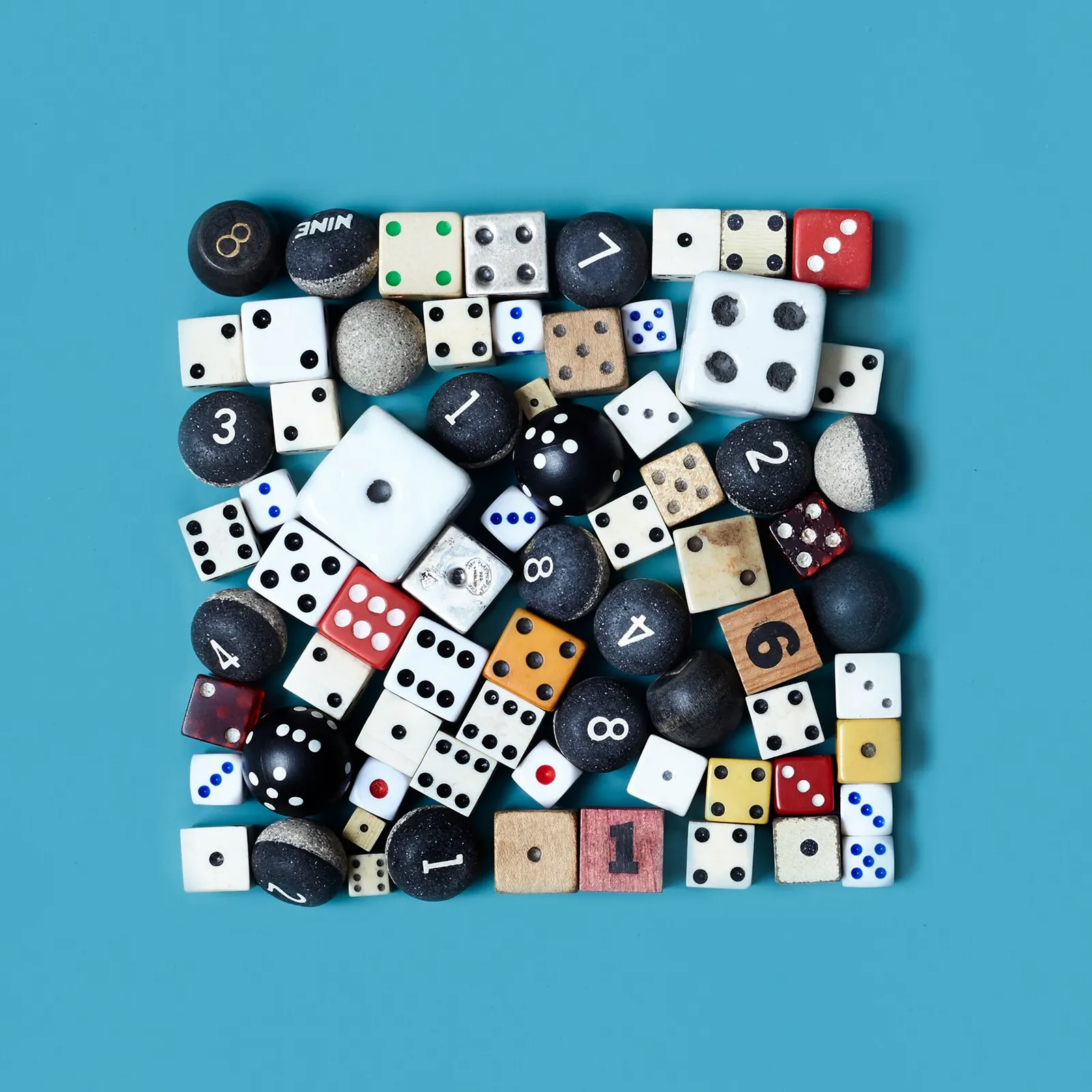 square collection of dice in many colors and sizes, with black numbered balls, on a teal background