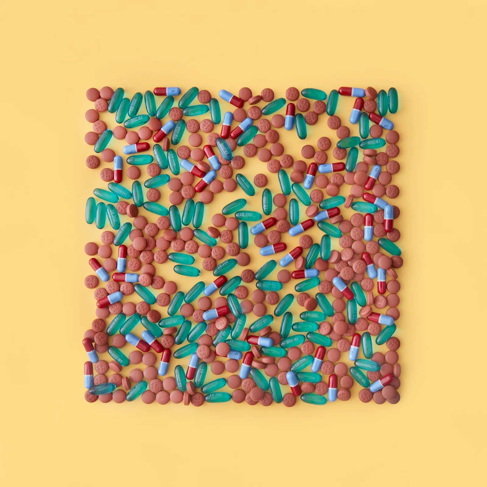 square of scattered round brown tablets, teal gel capsules and red and blue capsules on a pale yellow background