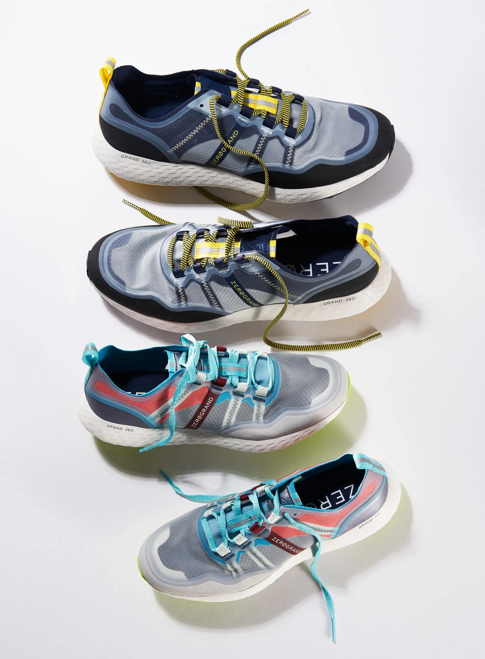 four mesh running sneakers in navy, gray and blue with yellow and teal laces, stacked at angles on white