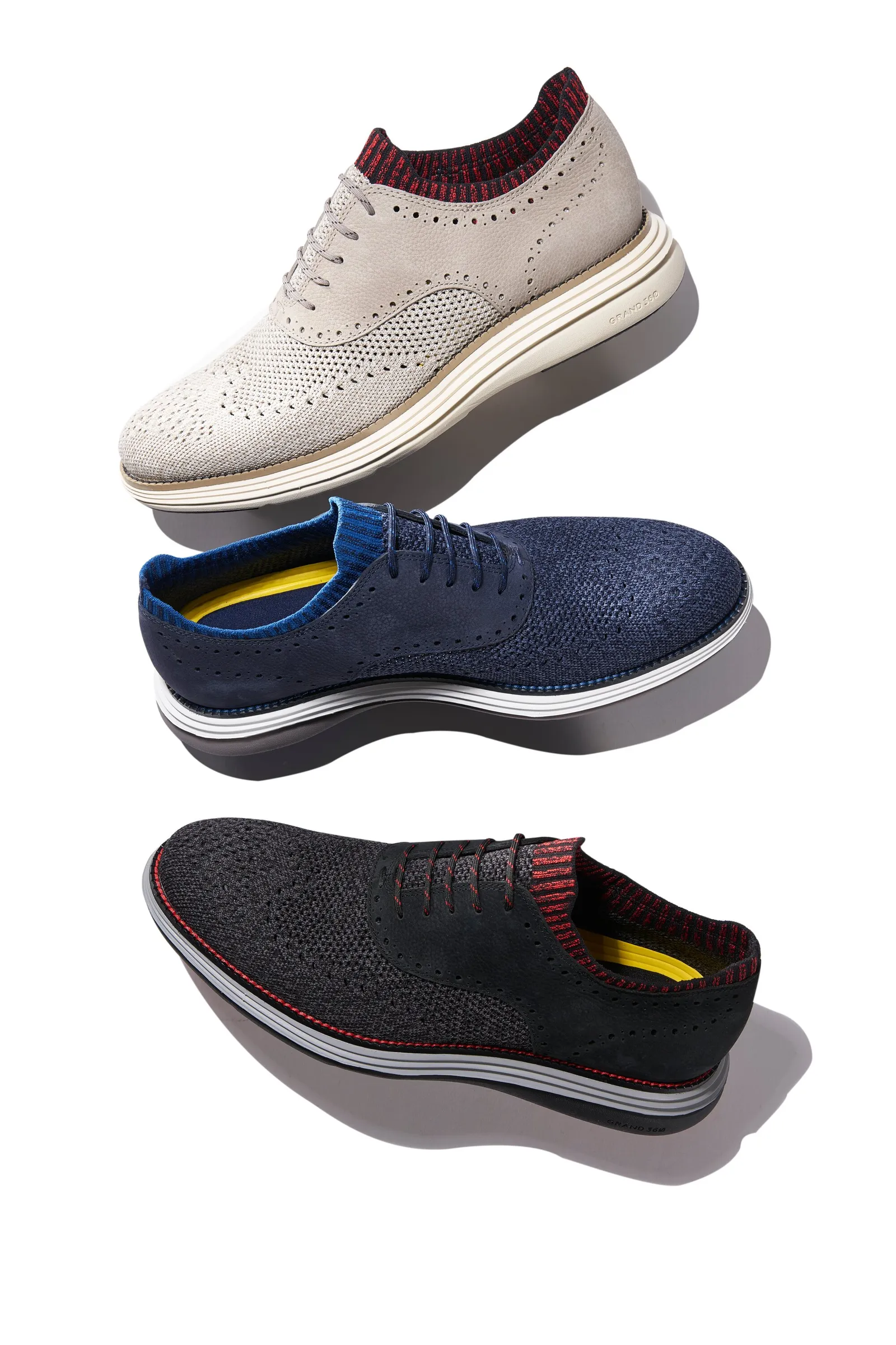 three knit wingtip oxfords in light gray, navy and black, floating one above another on white