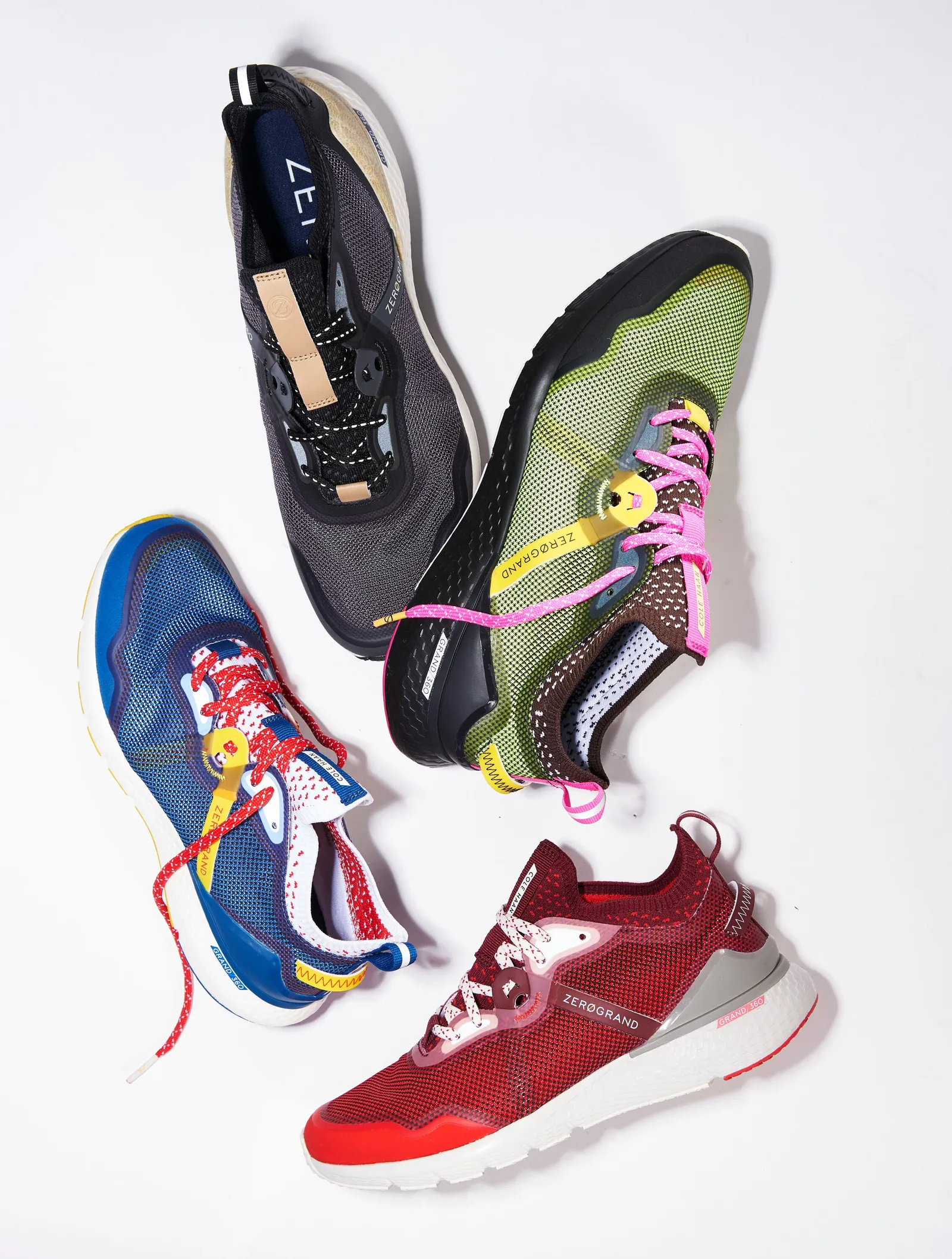 four colorful trail sneakers, black, lime green, cobalt blue and red, scattered at angles with bright pink and red laces