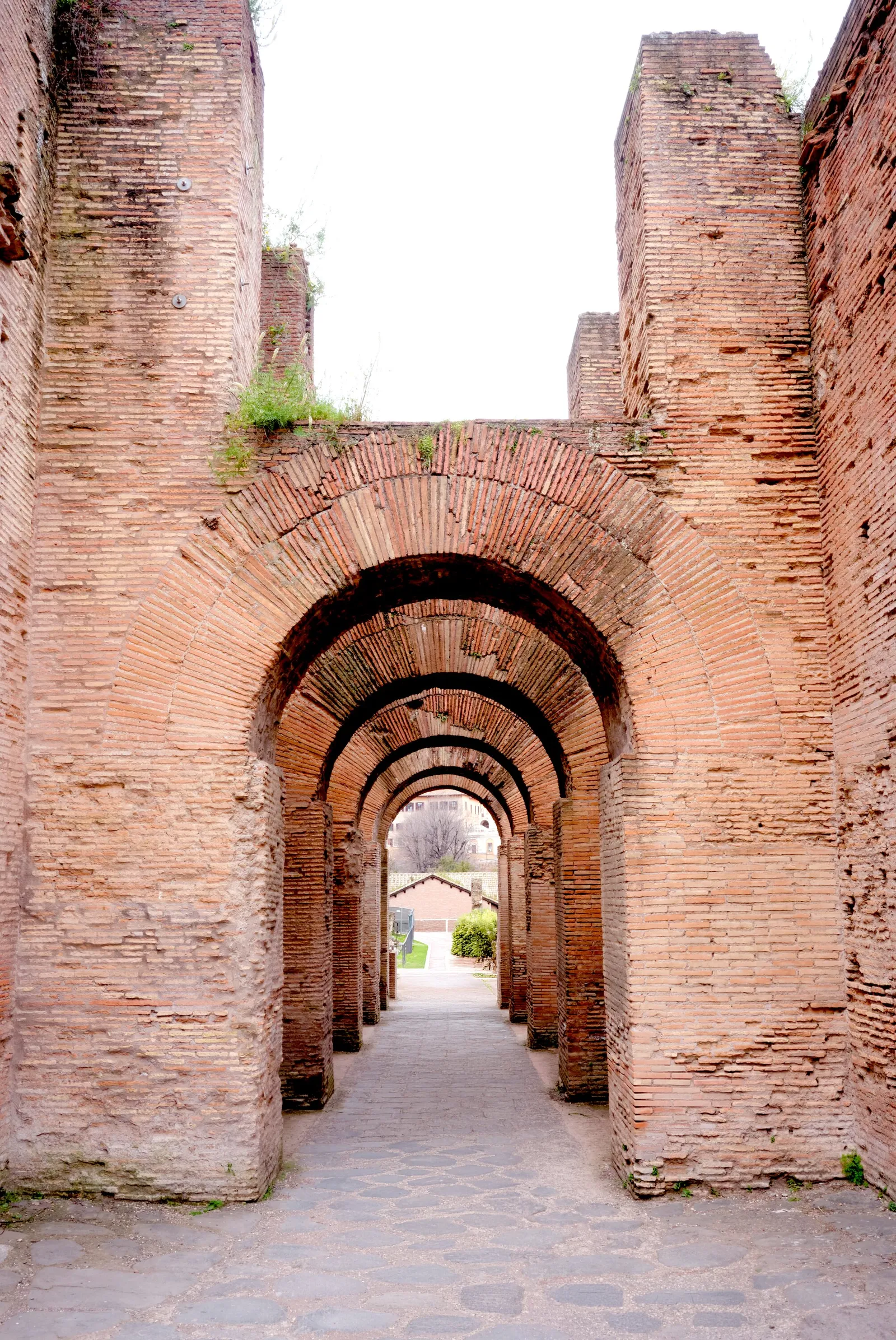 receding brick arches in a weathered pink-orange wall, with a cobbled passage leading to a small courtyard and trees beyond