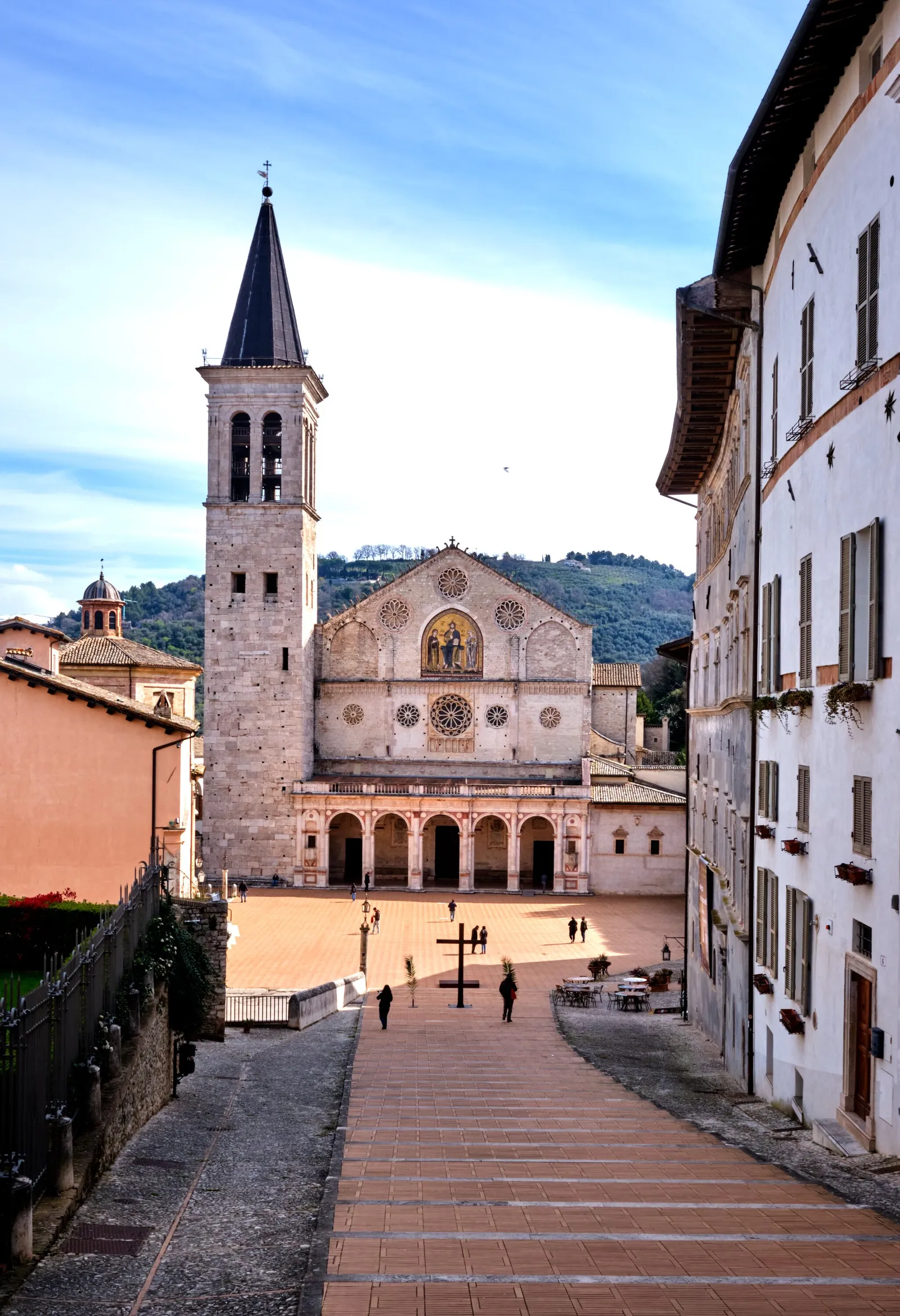 pink and white cathedral facade with a tall bell tower across an empty brick piazza, framed by a plaster building at right